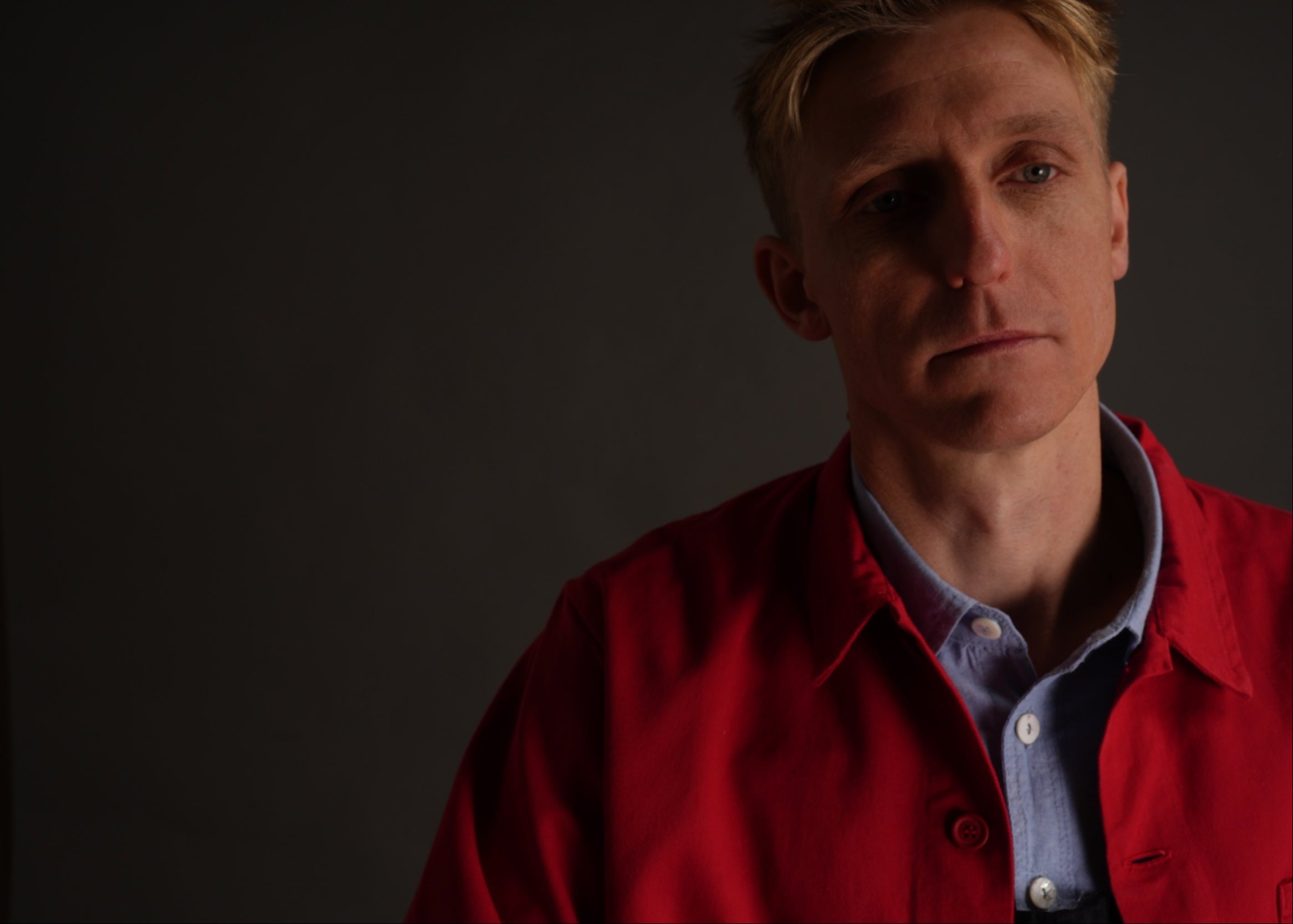 Tommy wears Carrier Company red garment washed cotton work jacket over navy blue dungarees and pale blue chambray shirt with no socks and white plimsoles