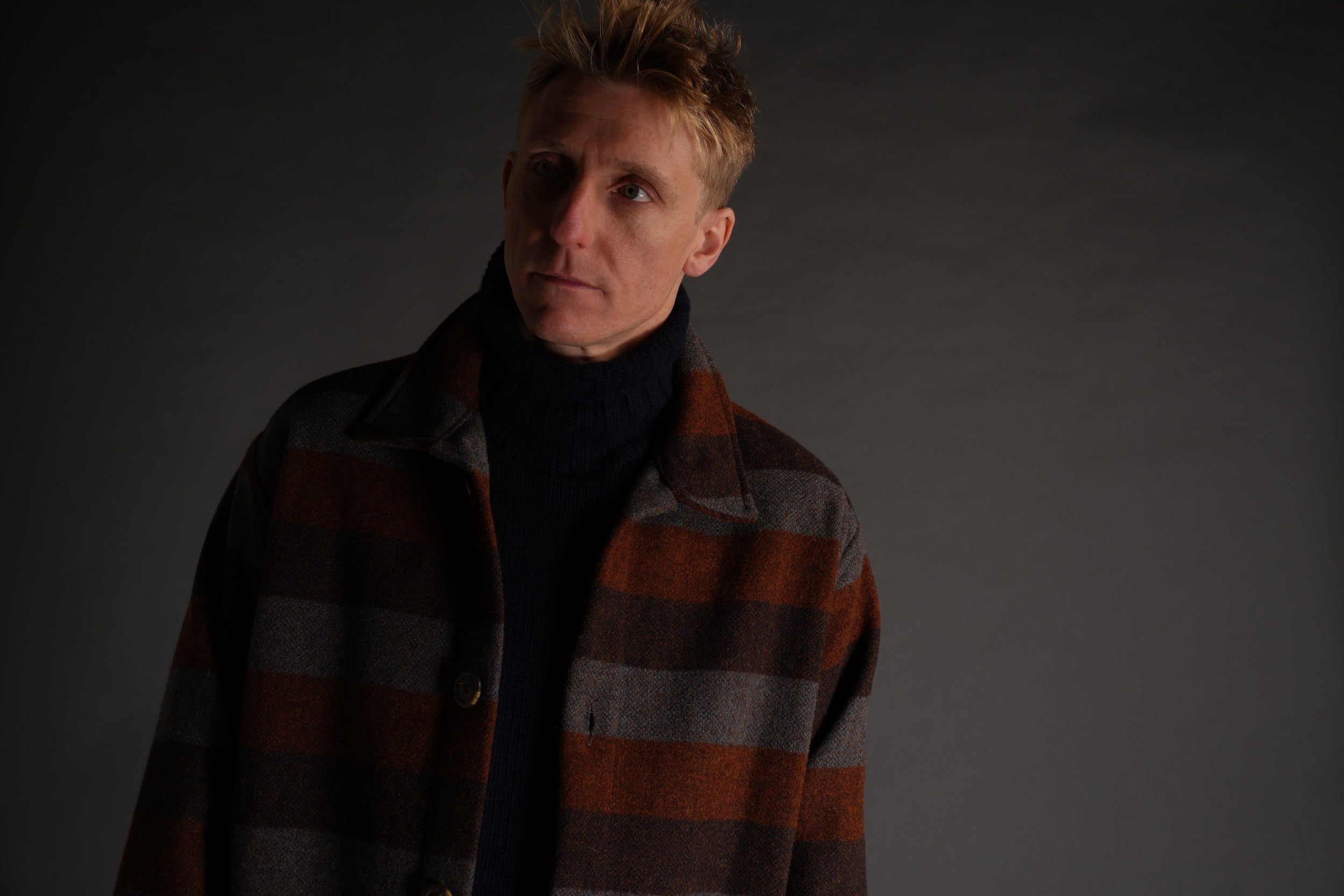 Tommy wears Conker striped wool jacket with navy roll neck jumper