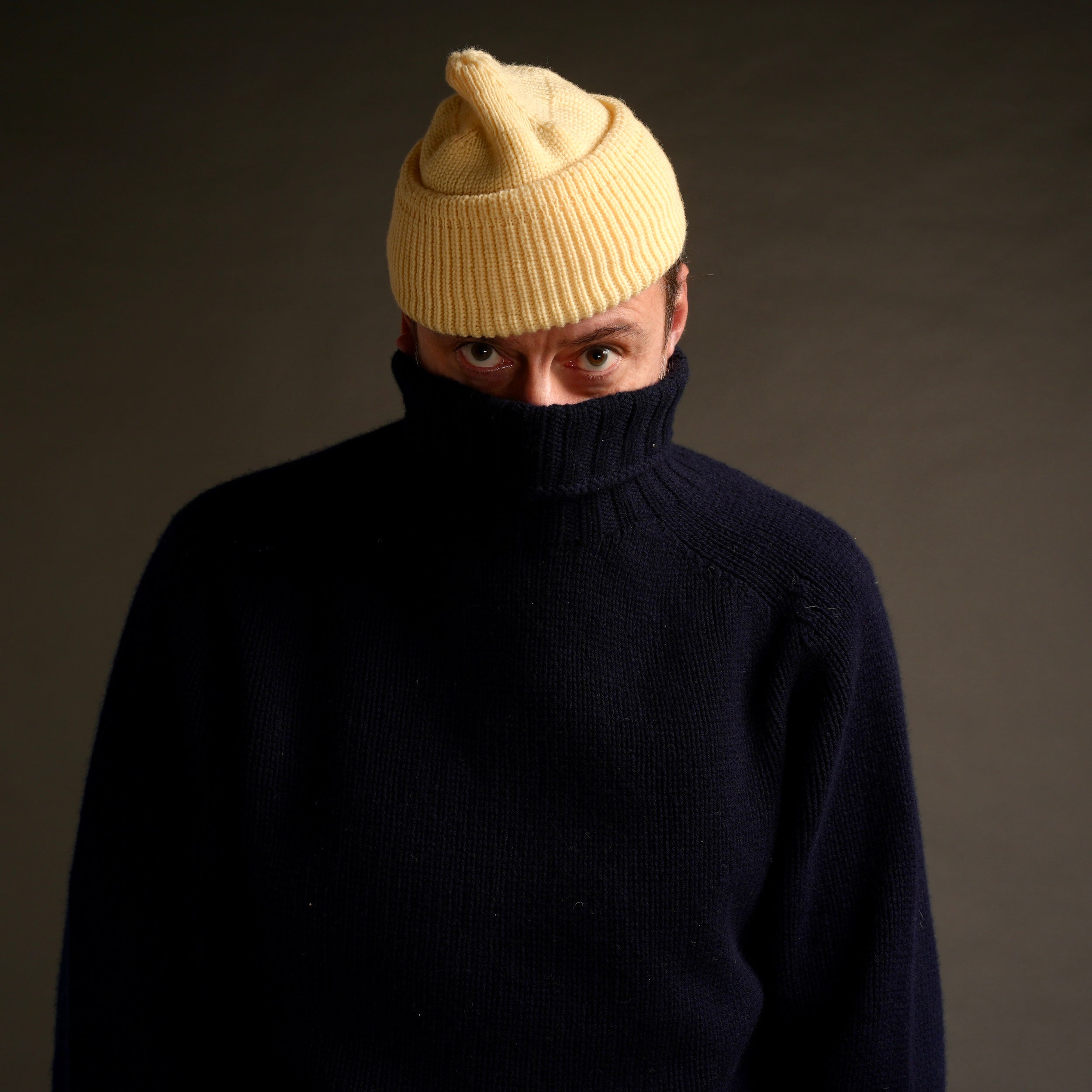 Enzo wears Navy Rollneck Supersoft Shetland jumper with Merino Watch Cap in Guava.