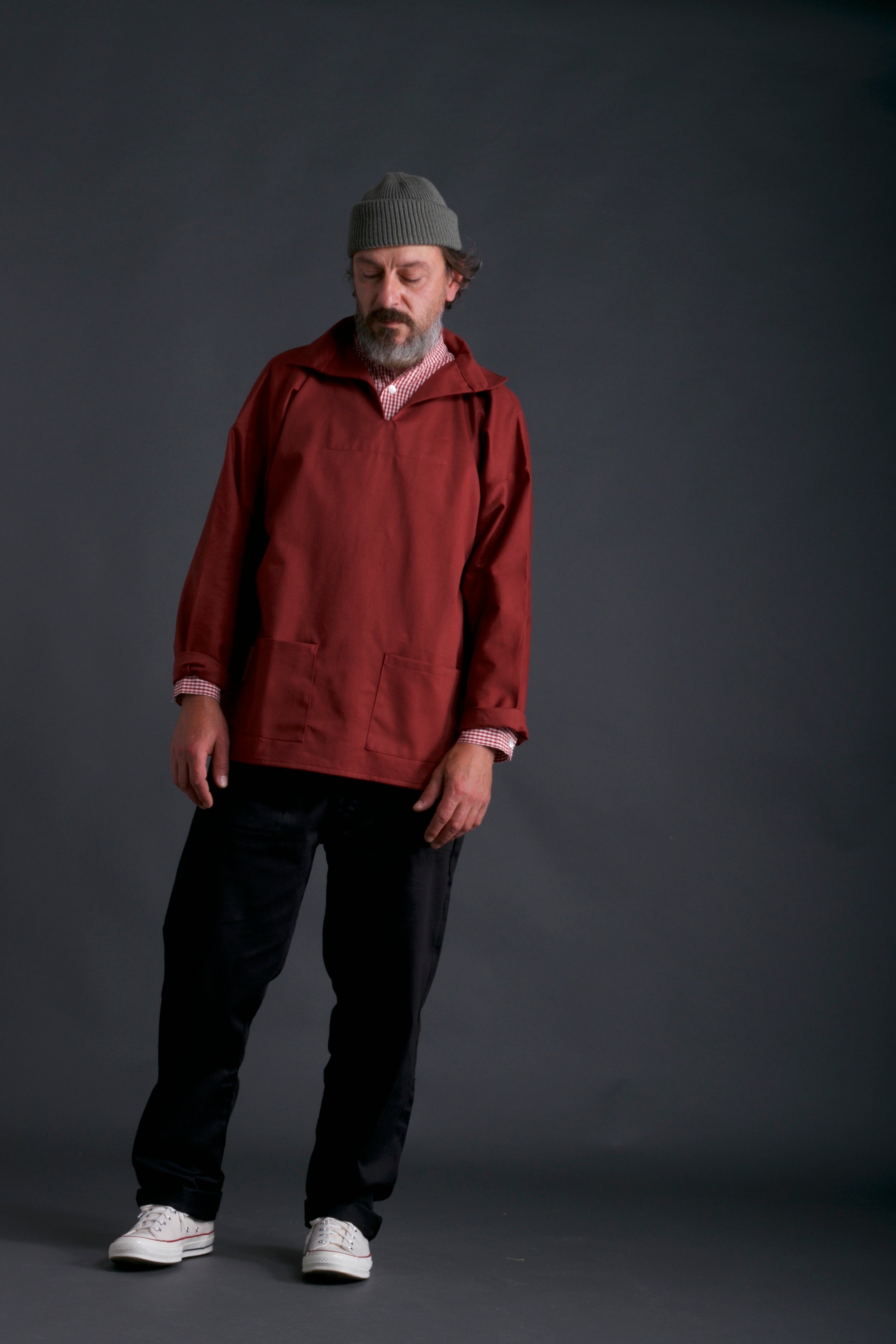 Man wears Carrier Company V-Neck Smock in Terracotta with Work trouser in Black and Wool Hat in Olive Drab