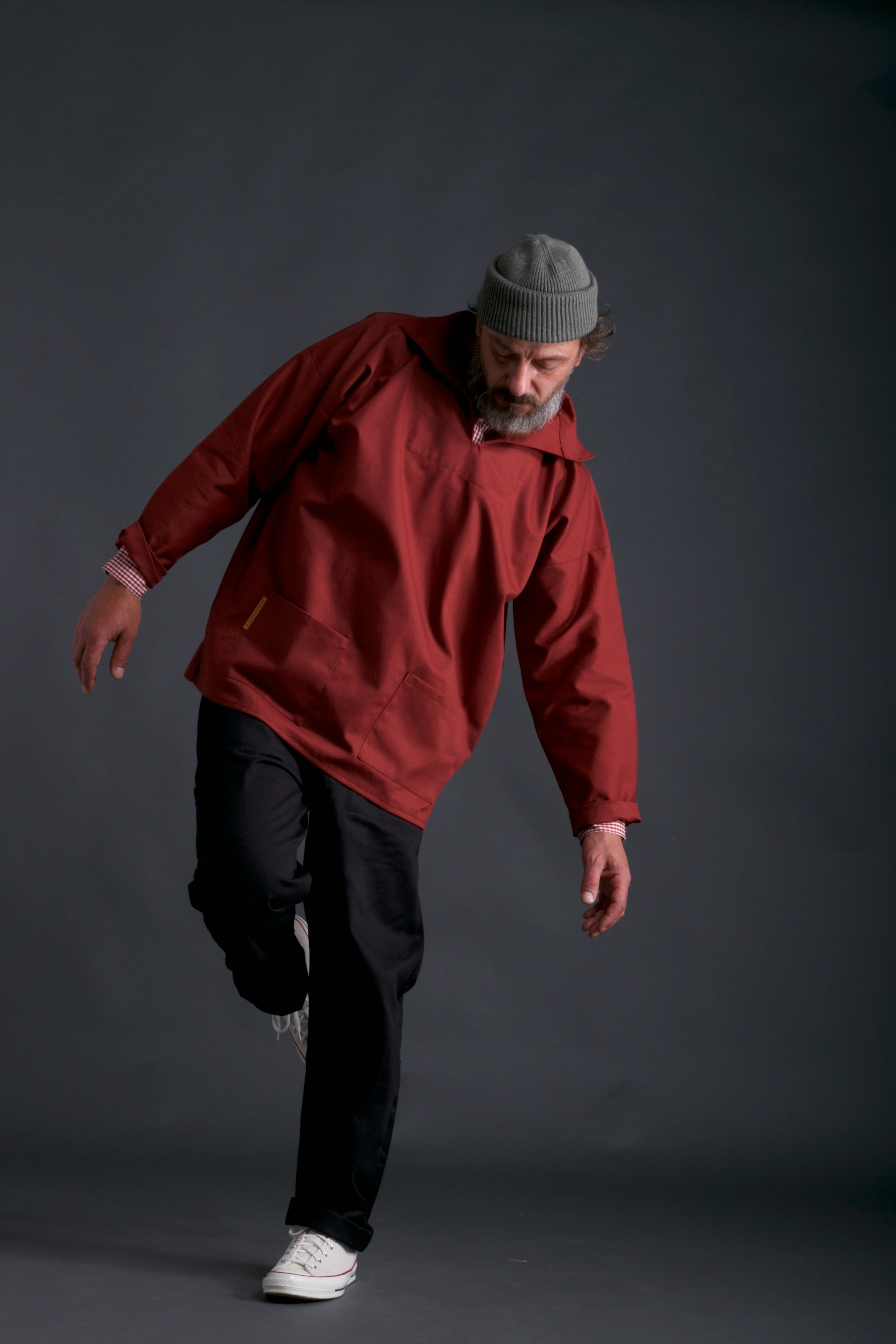 Man wears Carrier Company V-Neck Smock in Terracotta with Work trouser in Black and Wool Hat in Olive Drab