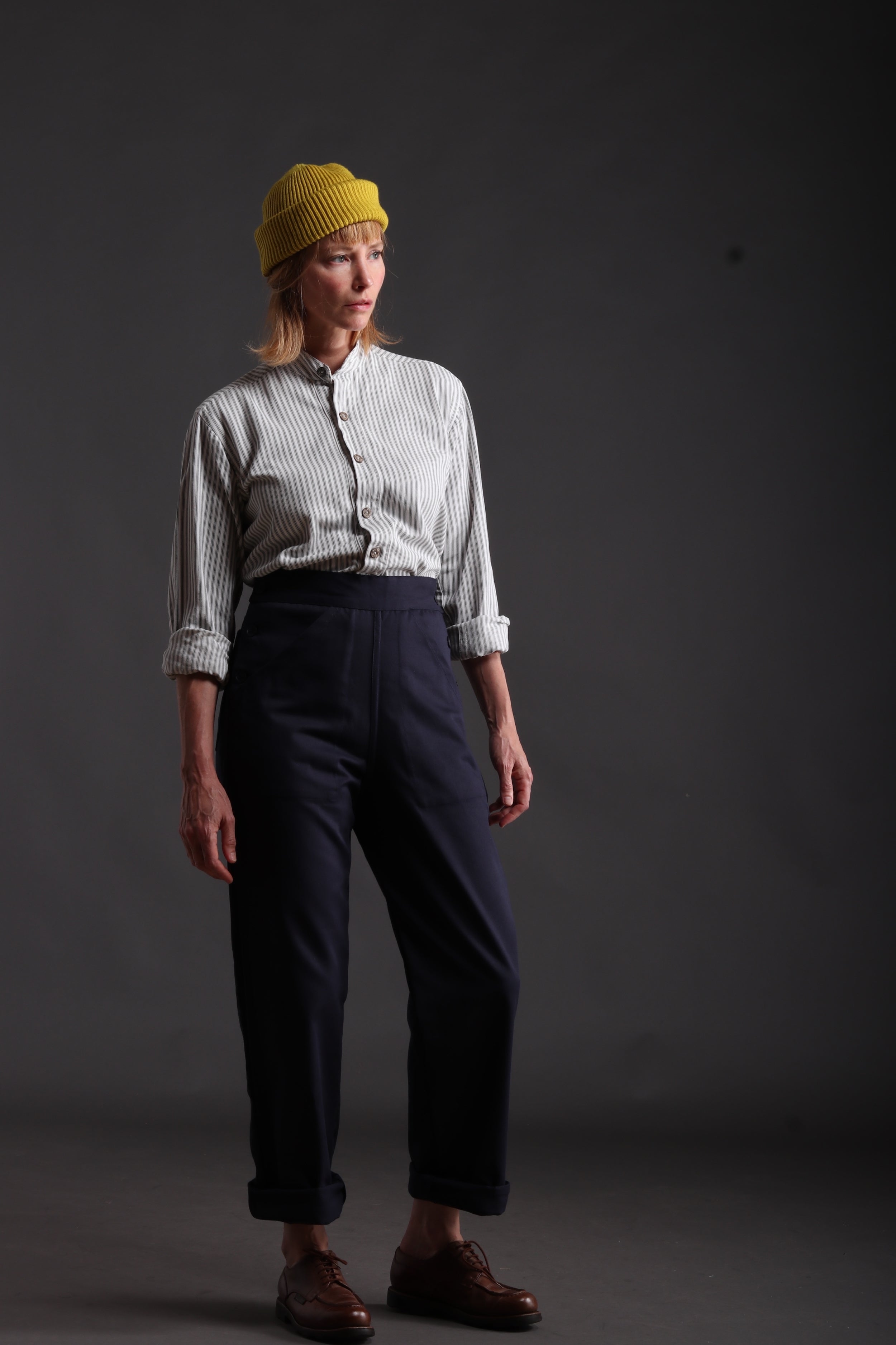 Woman wears Carrier Company Women's Work Trouser in Navy with Ticking Collarless Work Shirt and Wool Hat in Yellow