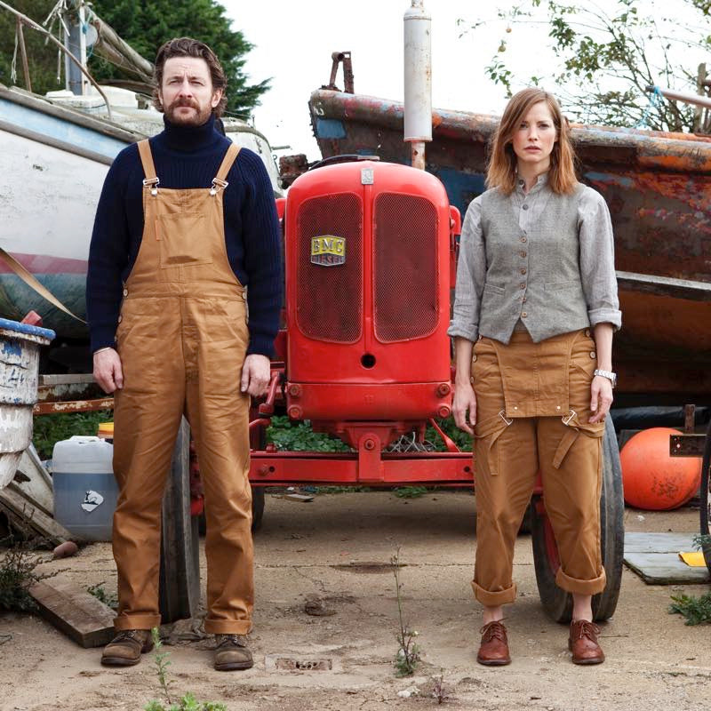Man and woman standing outside in front of a red tractor wearing the Carrier Company Men's Dungarees in Tan