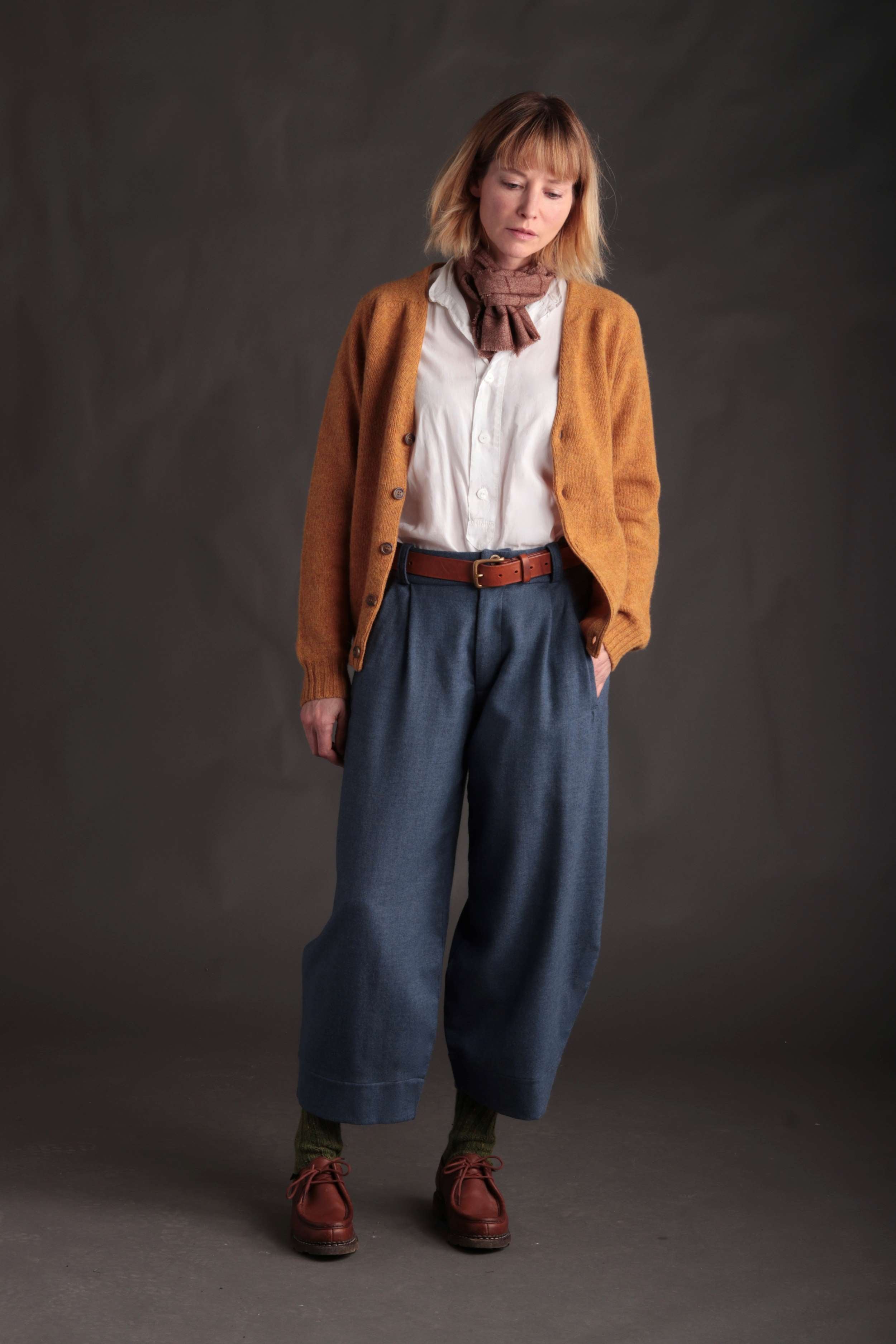 Woman wears Carrier Company Cardigan in Cumin with Dutch Trousers in Wool