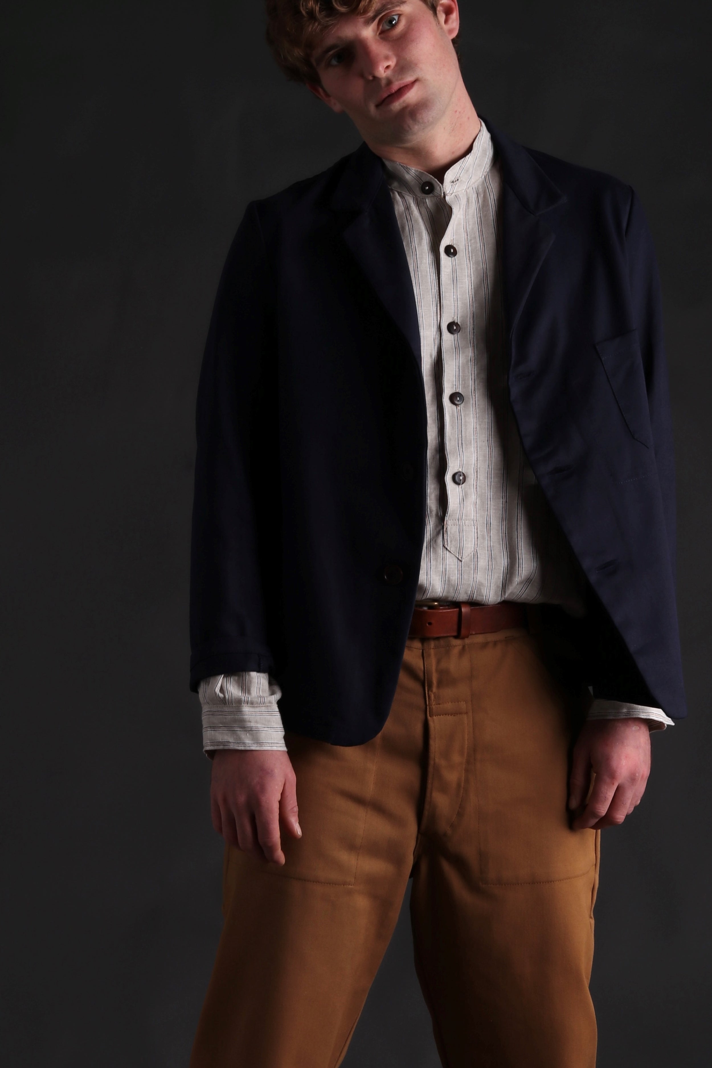 Man wears Carrier Company Collarless Shirt in Natural Linen with Three Button Navy Jacket and Tan Work Trousers
