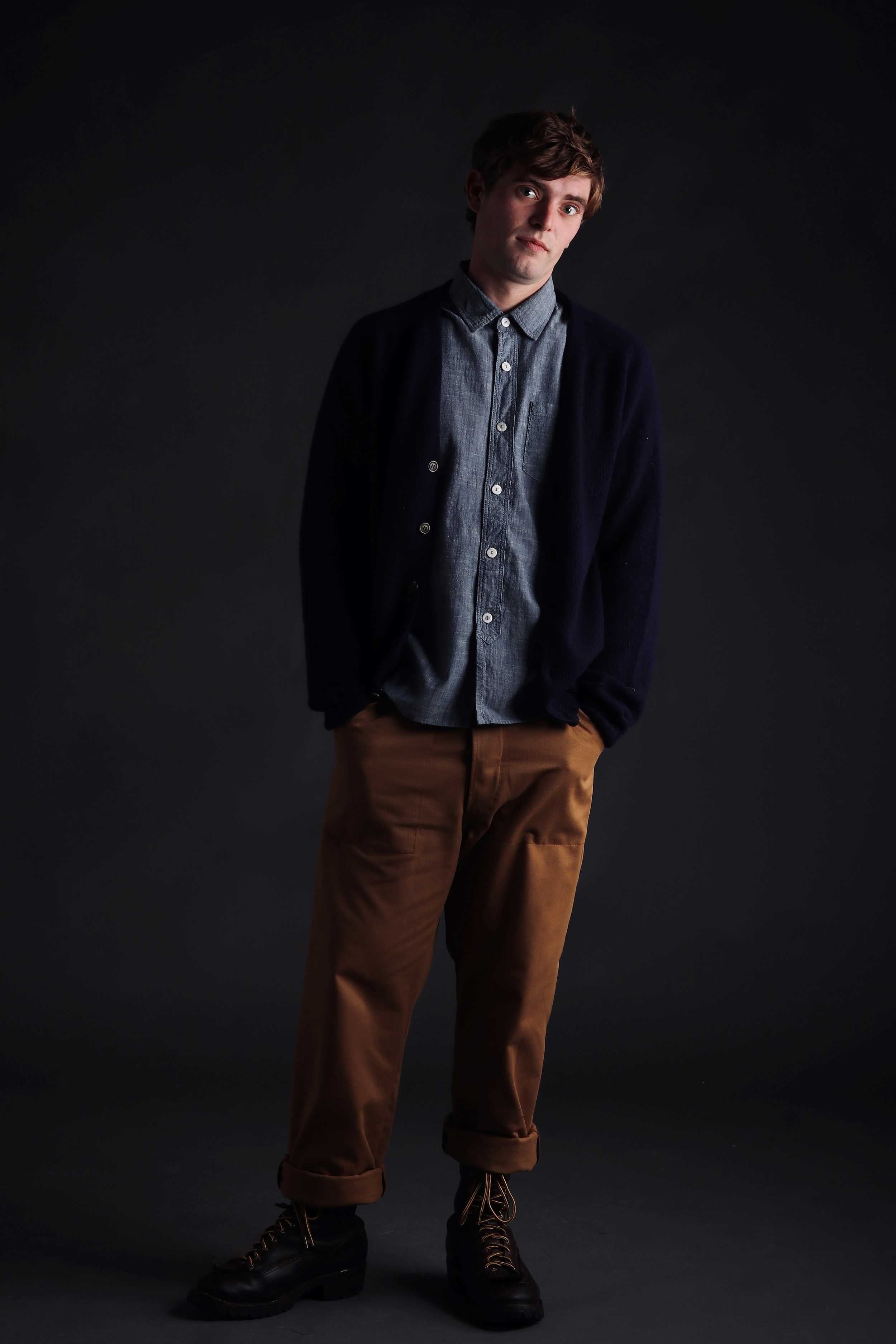 Man wearing Carrier Company Shetland Lambswool Cardigan in Navy with  Denim Shirt and Classic Work Trouser in Tan