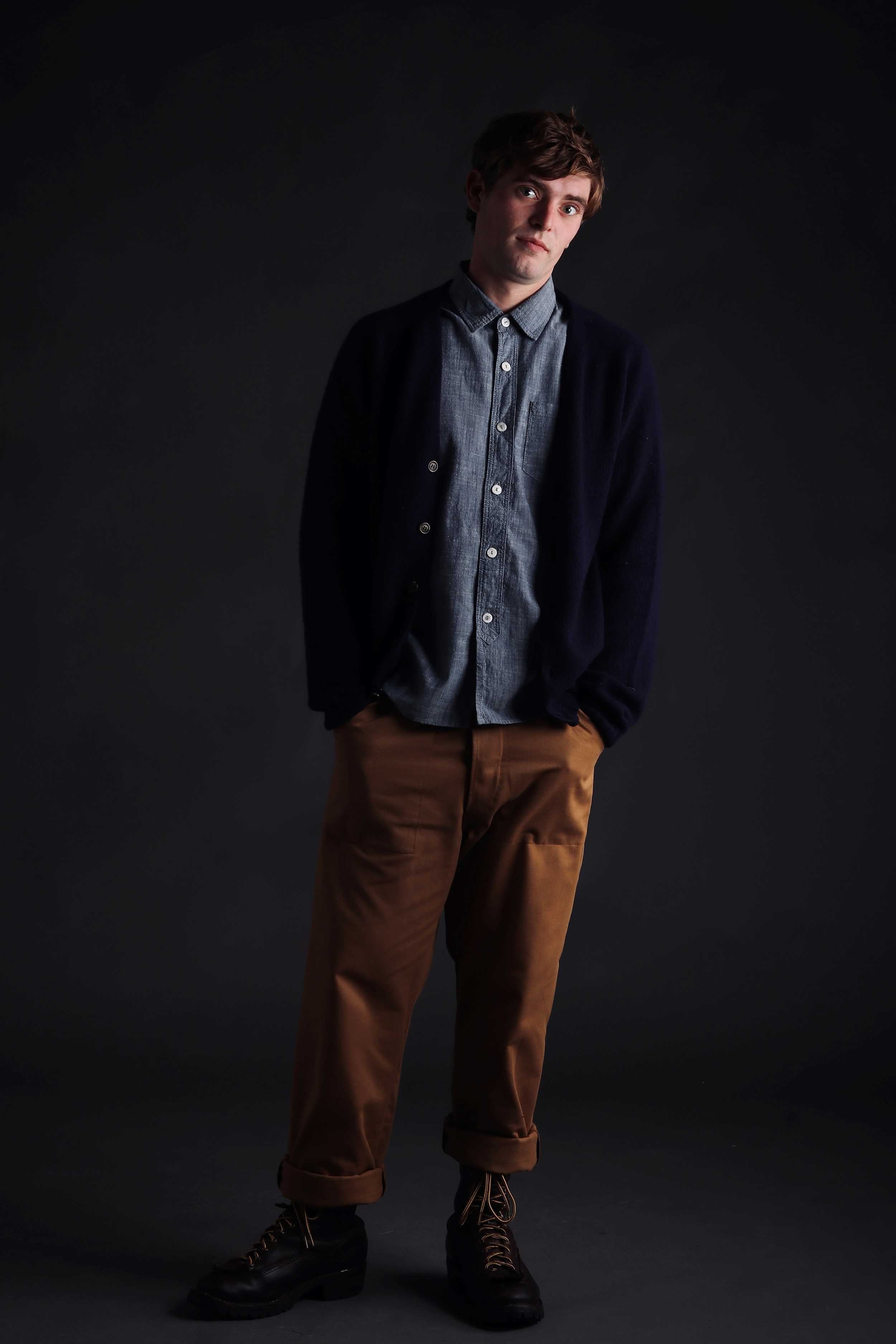 Man wearing Carrier Company Shetland Lambswool Cardigan in Navy with Denim Shirt and Classic Work Trouser in Tan