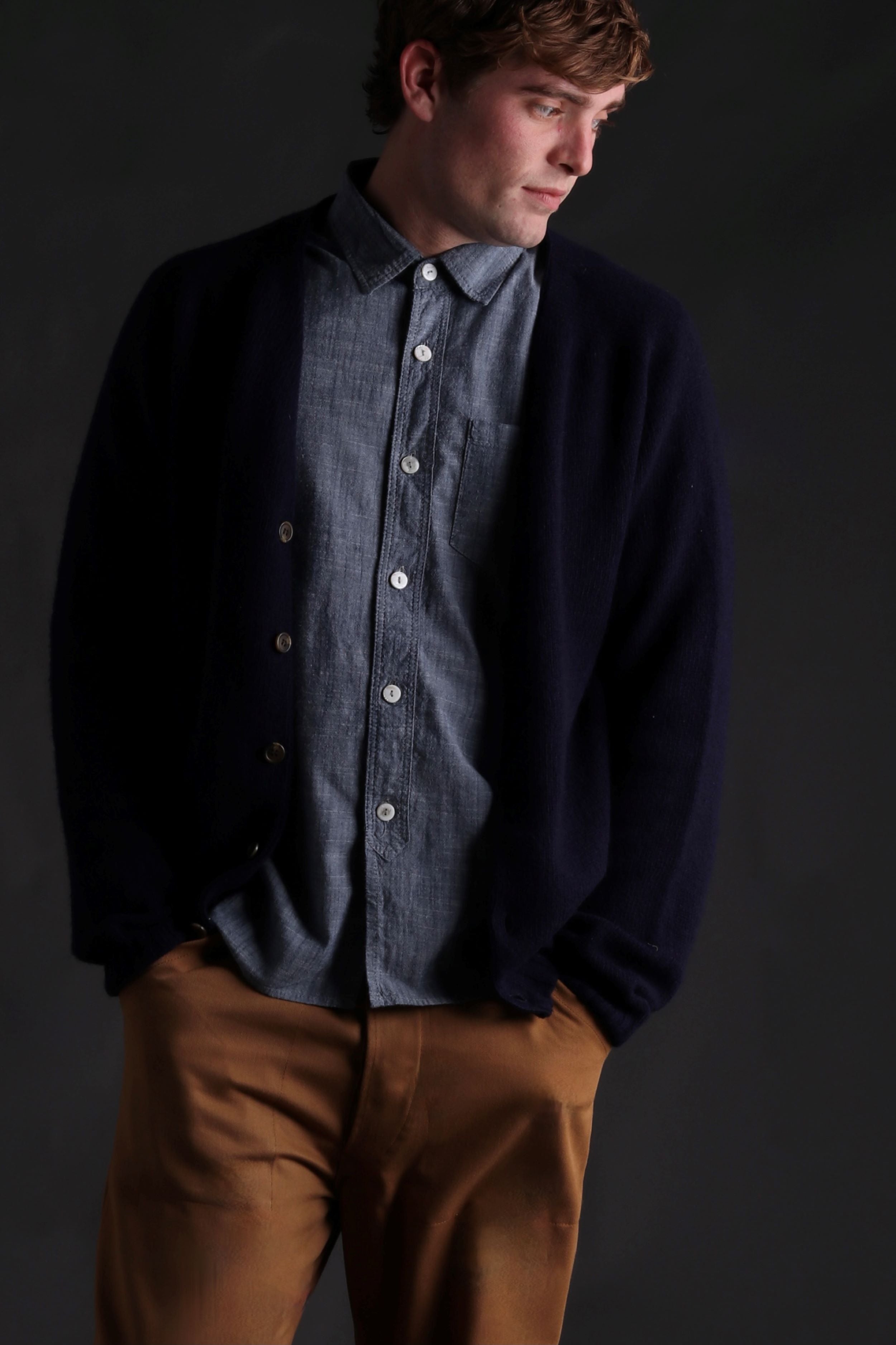 Man wearing Carrier Company Shetland Lambswool Cardigan in Navy with Denim Shirt and Classic Work Trouser in Tan
