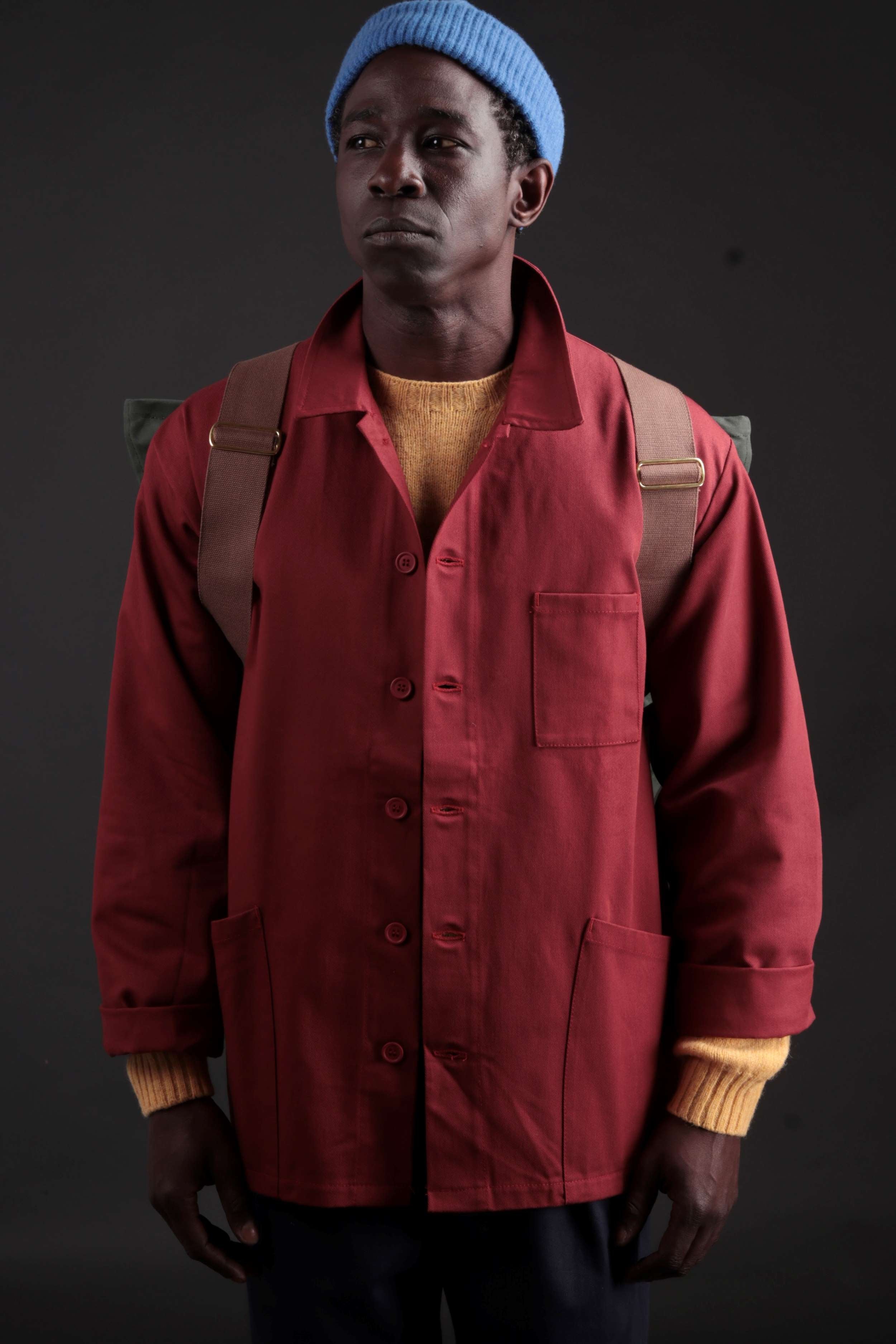 Man carries Carrier Company Backpack in Olive. Wearing Norfolk Work Jacket in Breton, Navy Classic Trousers and a Turquoise Donegal Hat