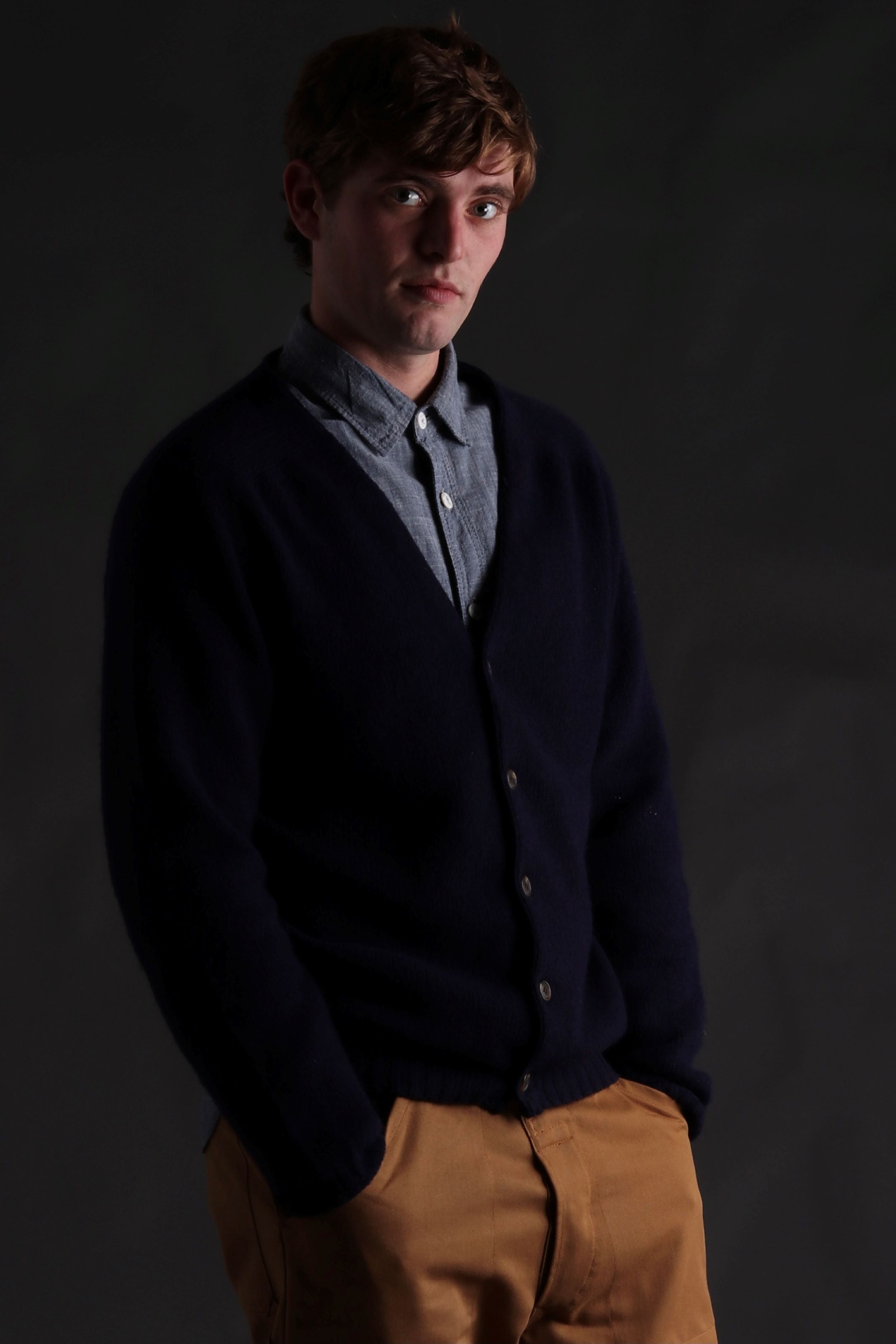 Man wearing Carrier Company Shetland Lambswool Cardigan in Navy with Denim Shirt and Classic Work Trouser in Tan