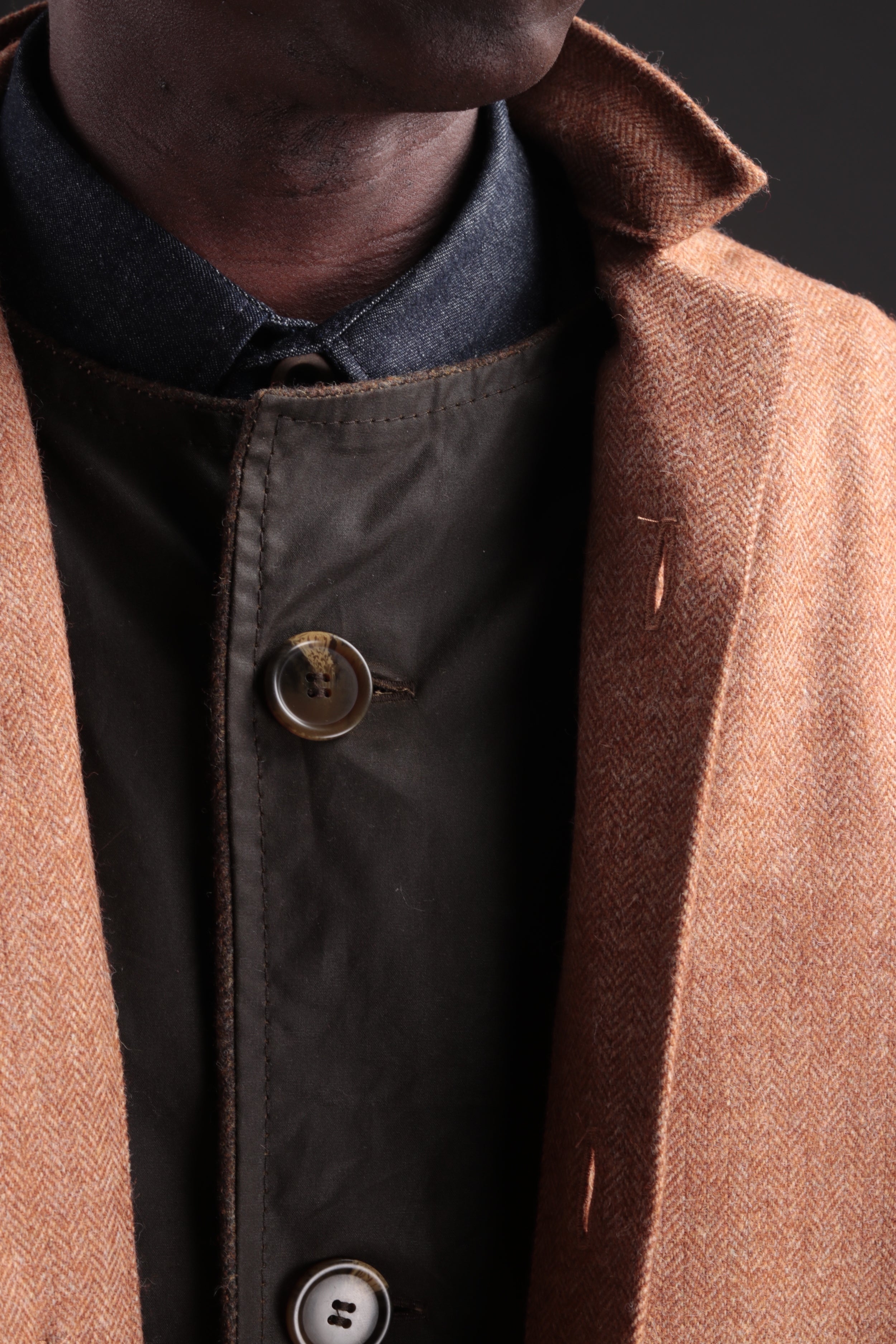 Man wears Carrier Company Tan Herringbone Wool Coat with Denim Collar Shirt and Norfolk Jerkin