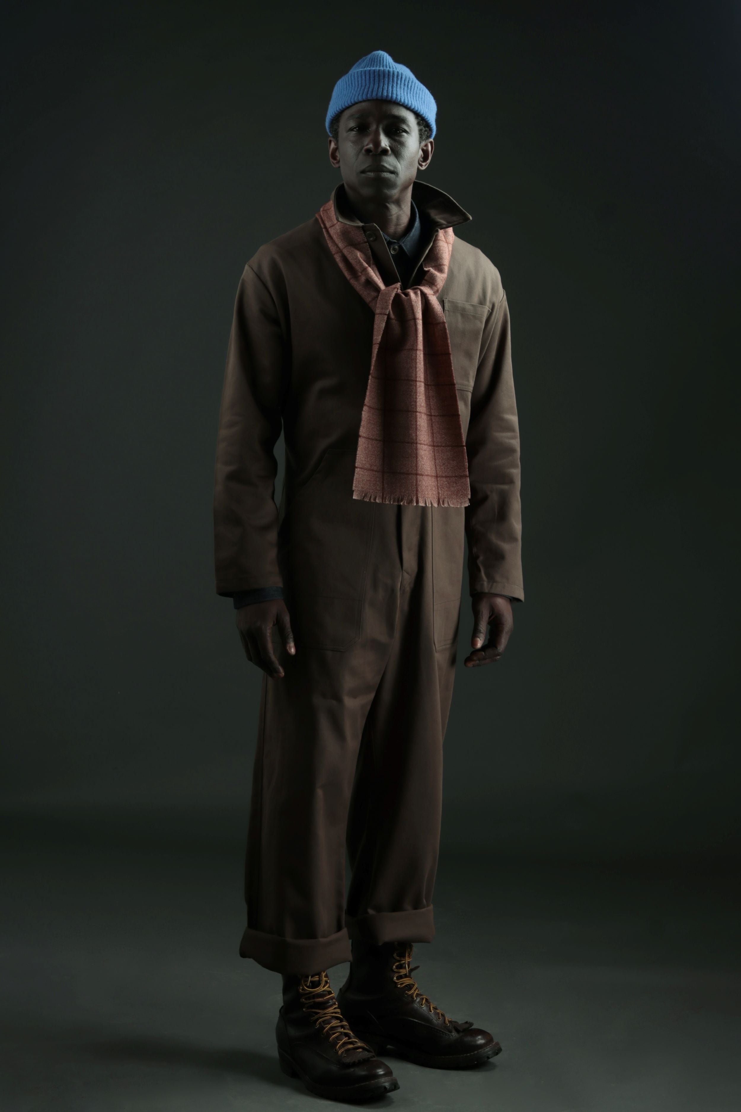 Man Wears Olive Boiler Suit with Check Short Scarf and Donegal Hat in Turquoise