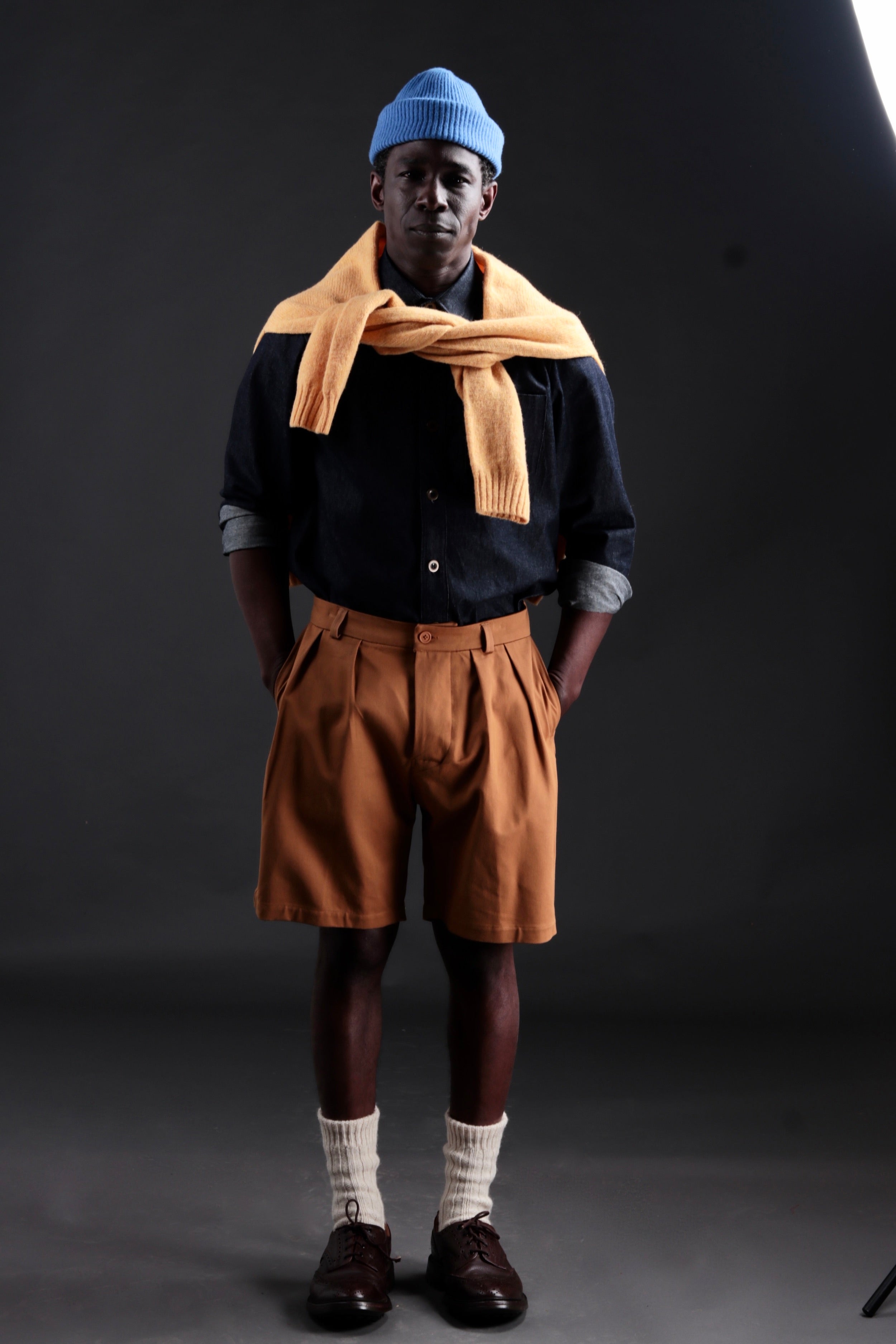 Abdul wears Carrier Company Grandpa Shorts in Tan with Denim Collar Shirt and Shetland Lambswool Jumper in Chamomile