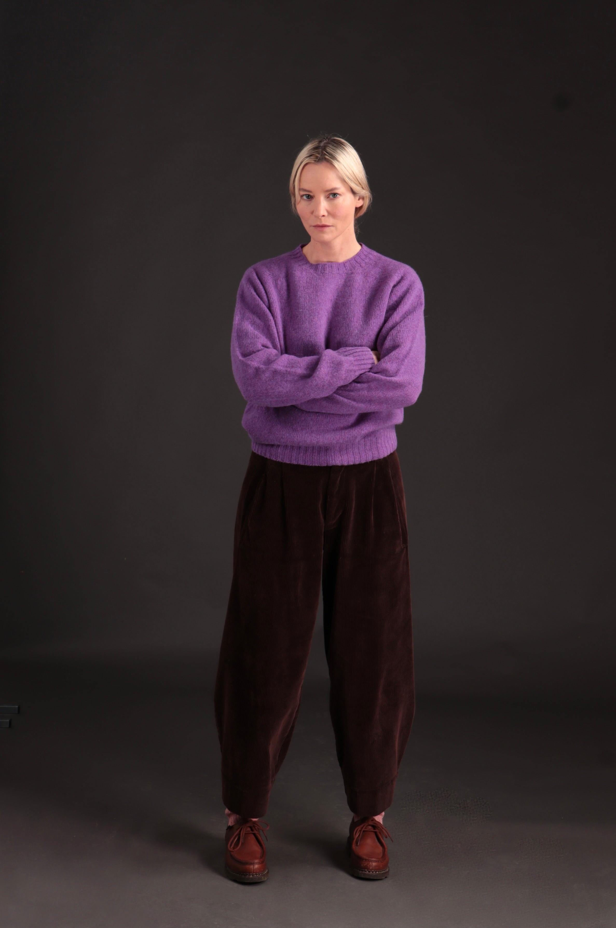 Woman wears Carrier Company Shetland Lambswool Jumper in Allium with Dutch Trouser in Chocolate Corduroy