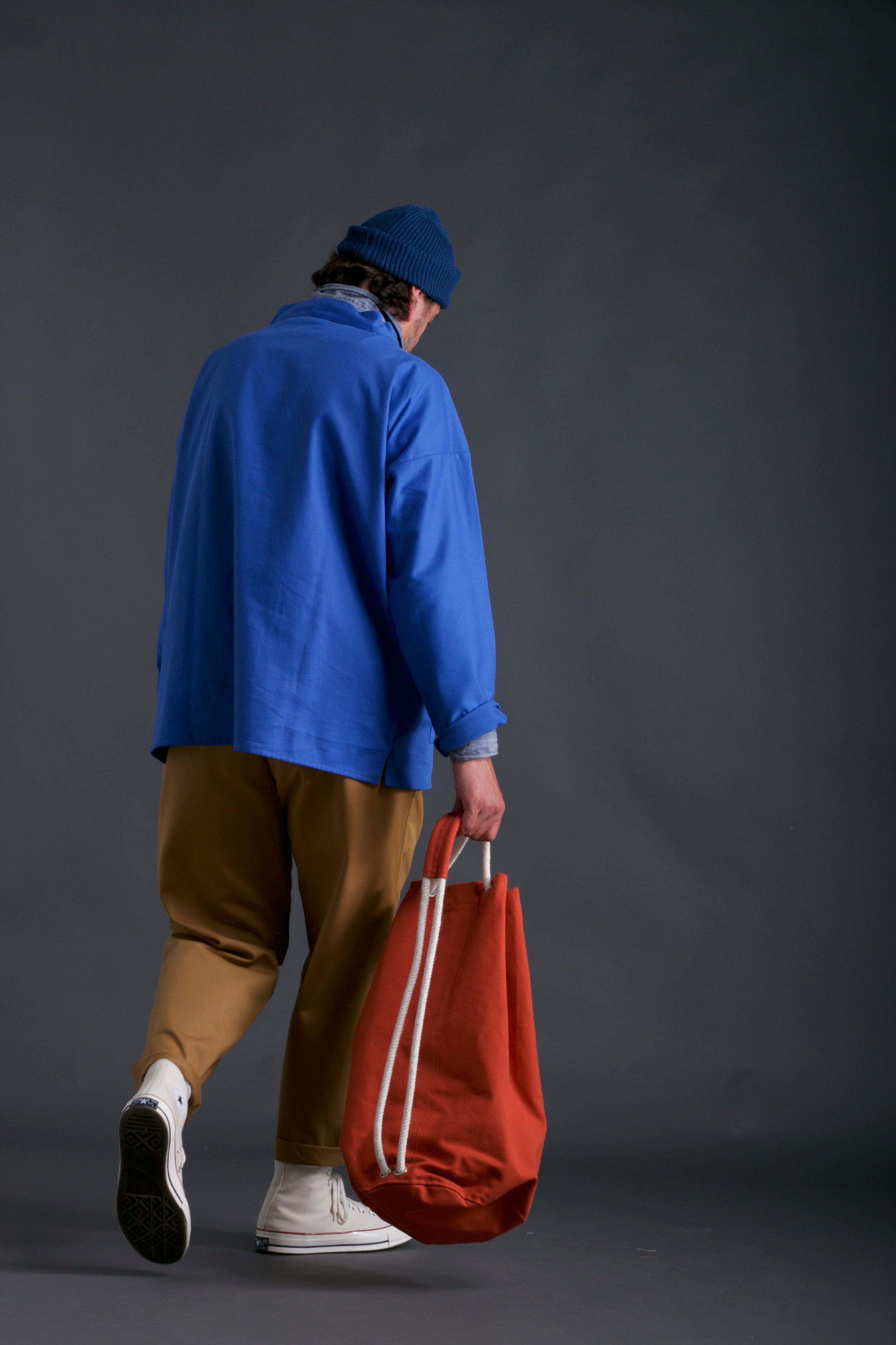 Man wears Carrier Company Traditional Slop in Sky, Classic Trouser, Chambray Shirt, Wool Hat and Carrier Company Duffel Bag in Orange