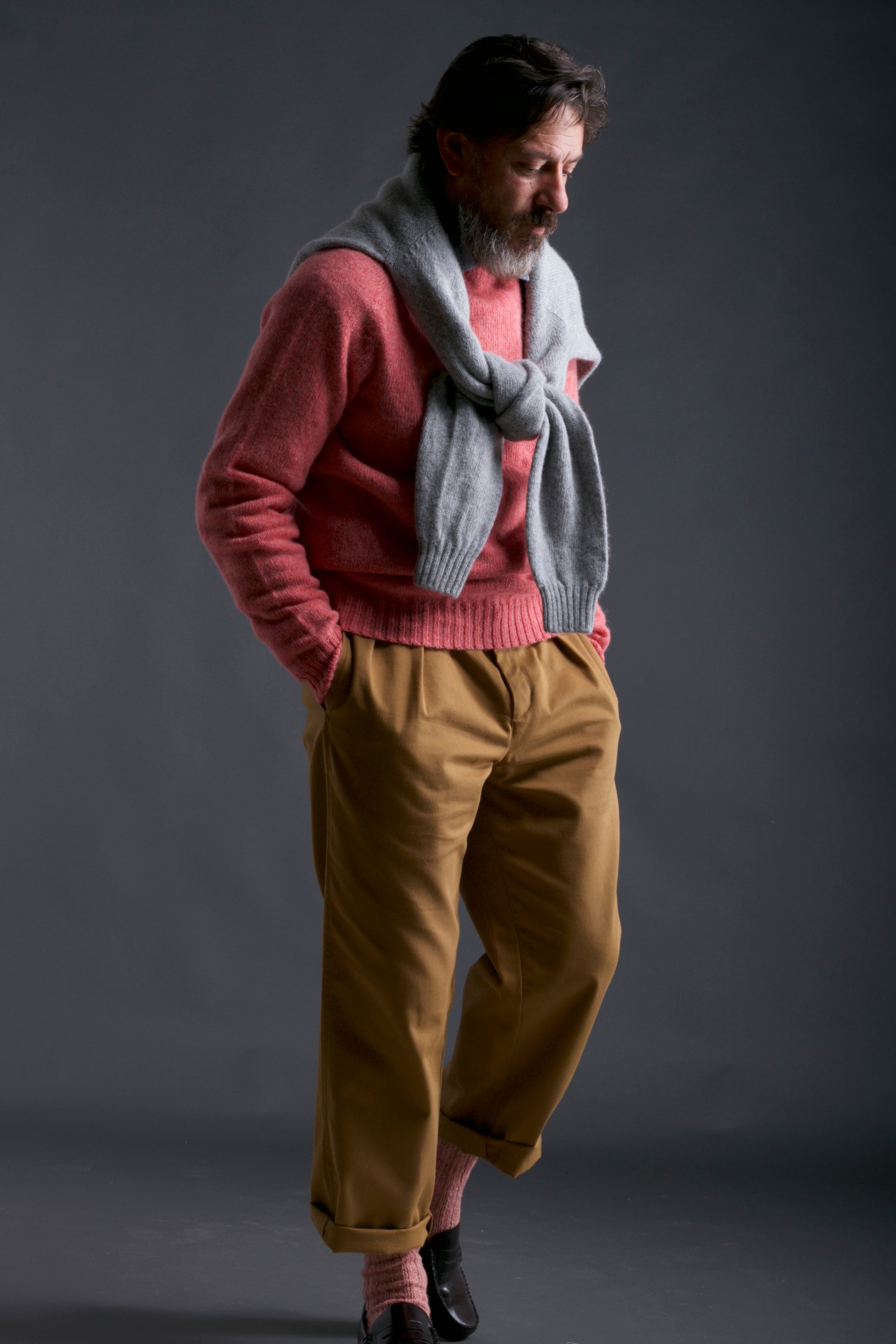 Man wears Carrier Company Shetland Lambswool Jumper in Salmon with Chambray Shirt and Classic Trouser in Tan