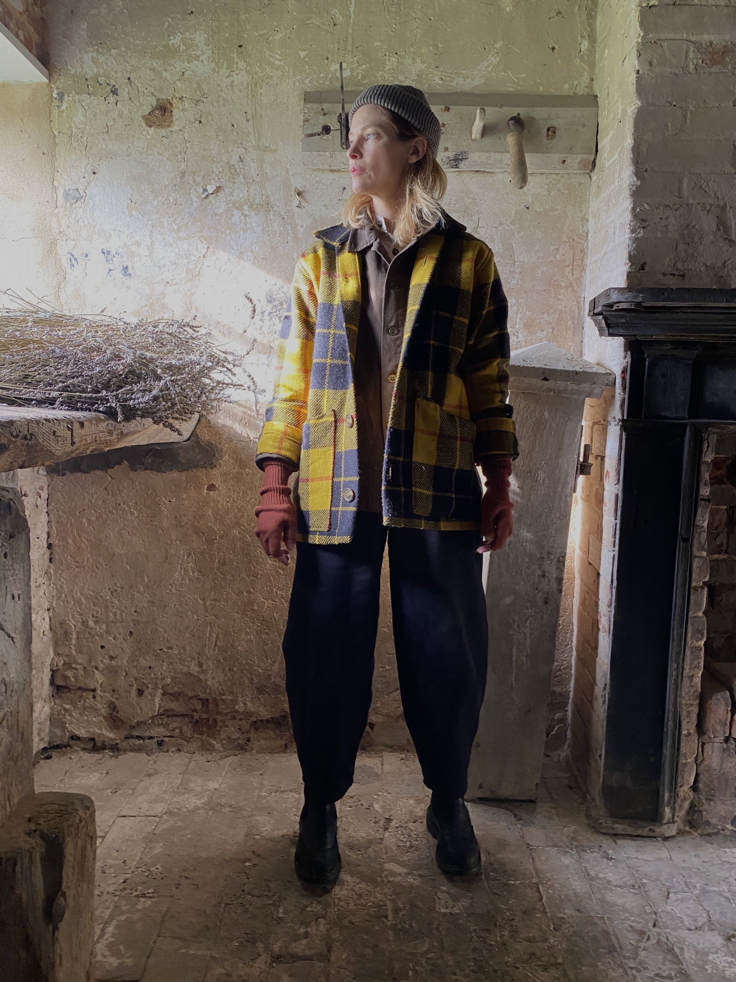 Woman in barn wearing Carrier Company Celtic Wool Jacket in Black and Yellow Check with Wool Hat and Black Dutch Trouser in Cotton Drill