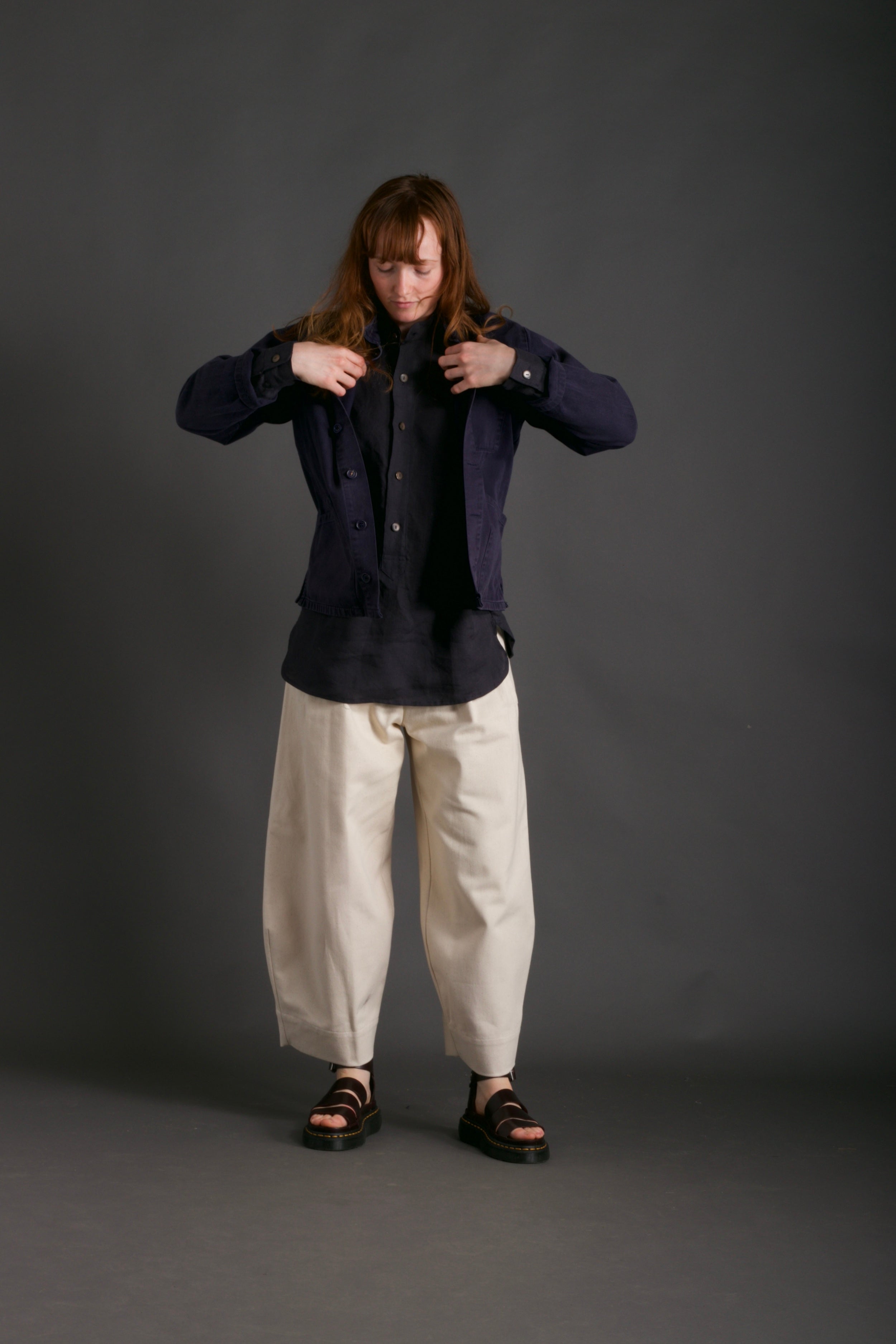 Woman wearing Carrier Company Traditional Norfolk Work Jacket in Navy with Dutch Trouser in Seeded Denim and Collarless Work Shirt in Navy Linen