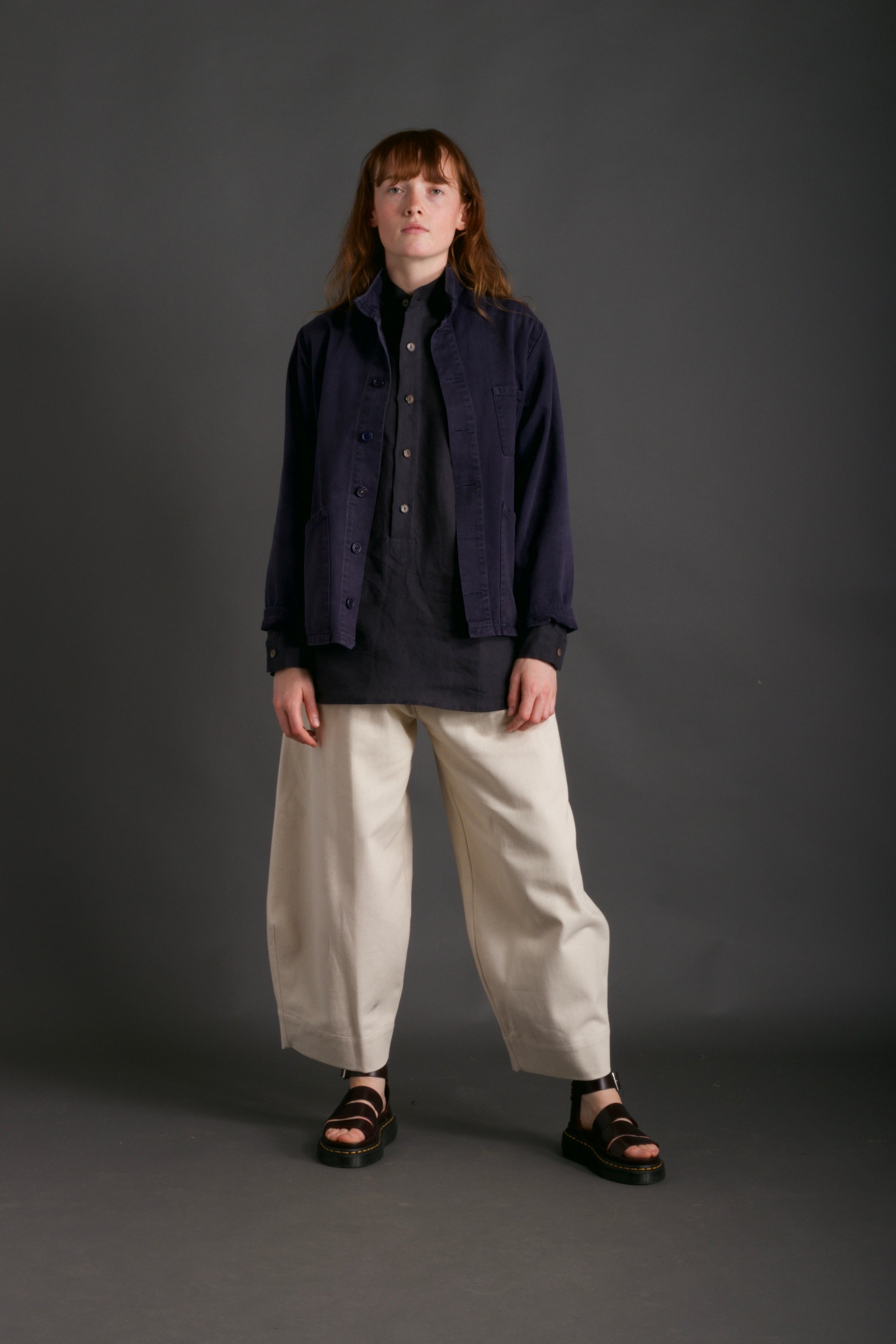 Woman wearing Carrier Company Traditional Norfolk Work Jacket in Navy with Dutch Trouser in Seeded Denim and Collarless Work Shirt in Navy Linen