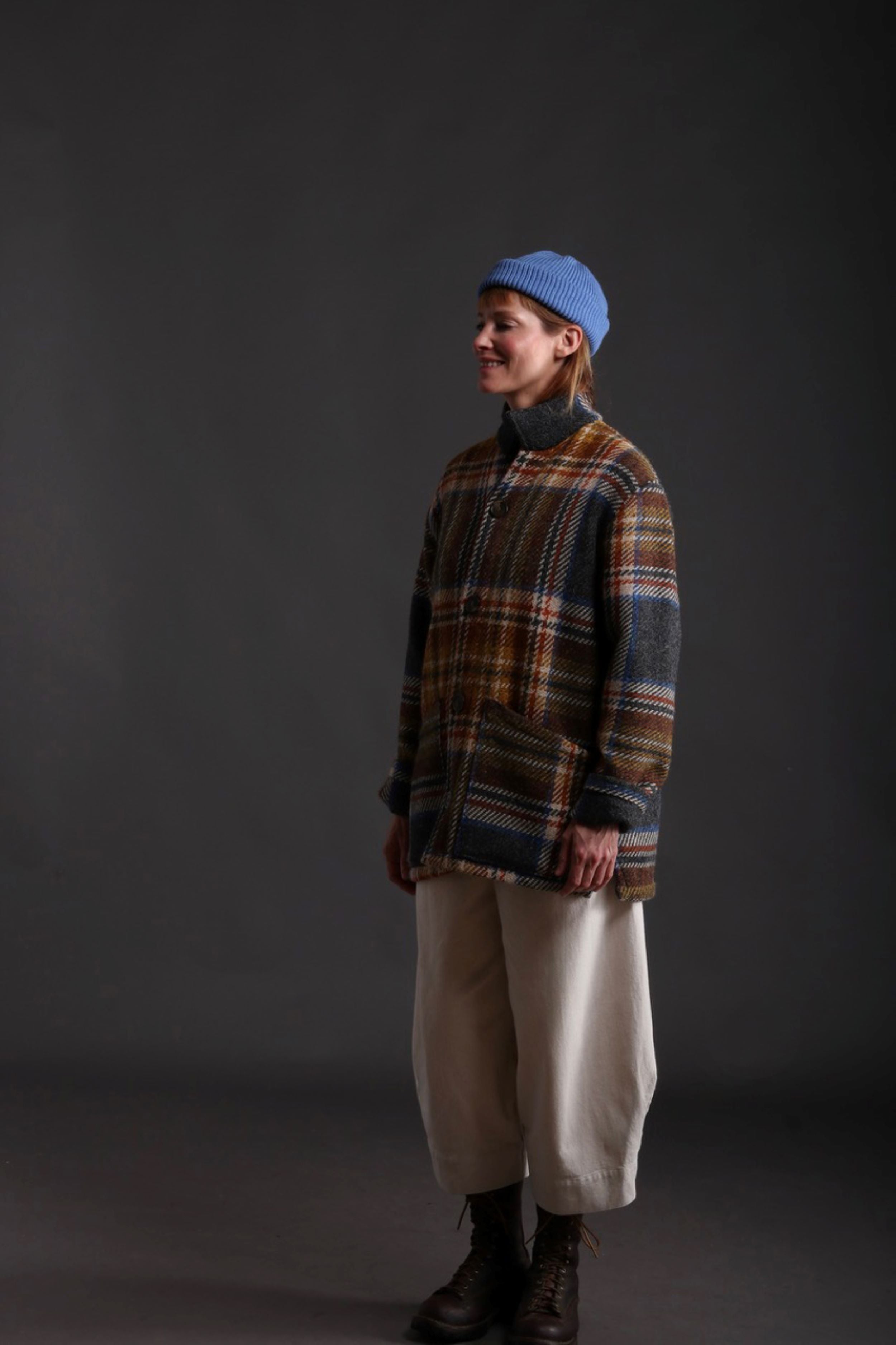 Woman wears Celtic Wool Jacket in Slate with Seeded Denim Dutch Trouser, Womens Waistcoat in Brown Wool, Collarless Work Shirt in Striped Linen and Merino Wool Hat in Sky Blue