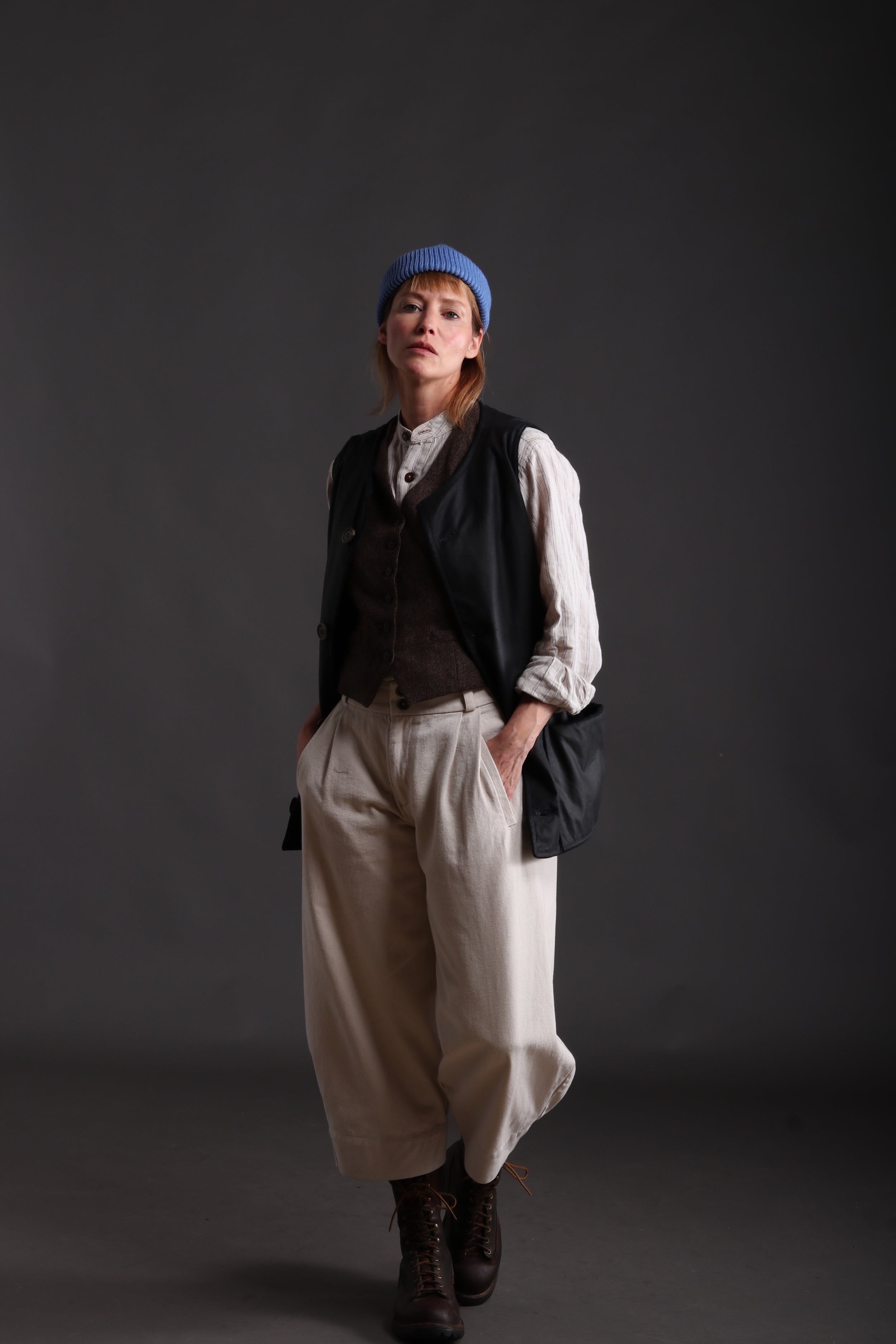 Woman wears Carrier Company Dutch Trouser in Seeded Denim with Linen Colarless Shirt, Women's Wool Waistcoat and  Wax Cotton Jerkin