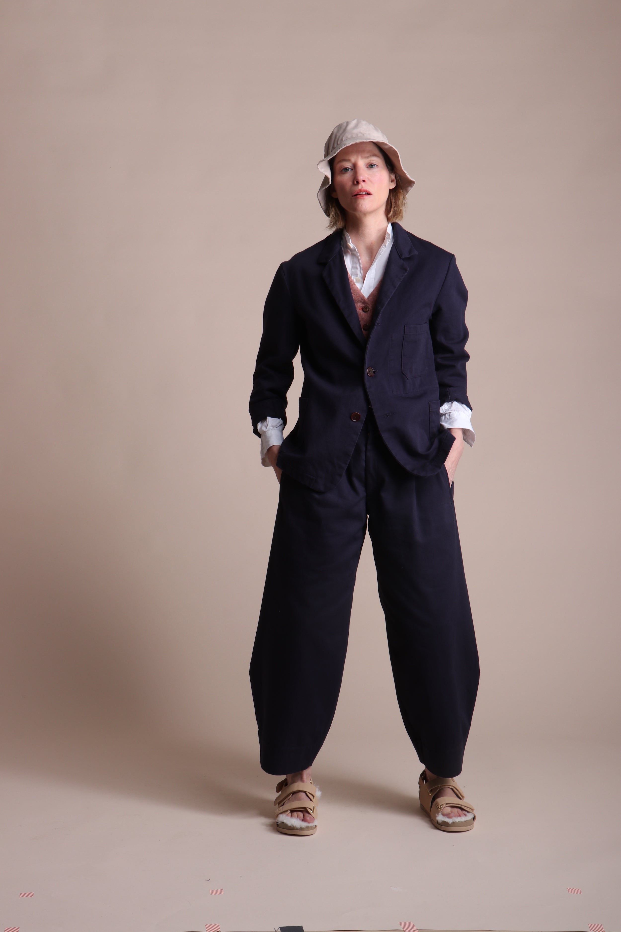 Woman wears Carrier Company 3 Button Jacket in Navy Drill with Dutch Trouser in Cotton, Lightweight Collarless Shirt and Wool Waistcoat in Coral