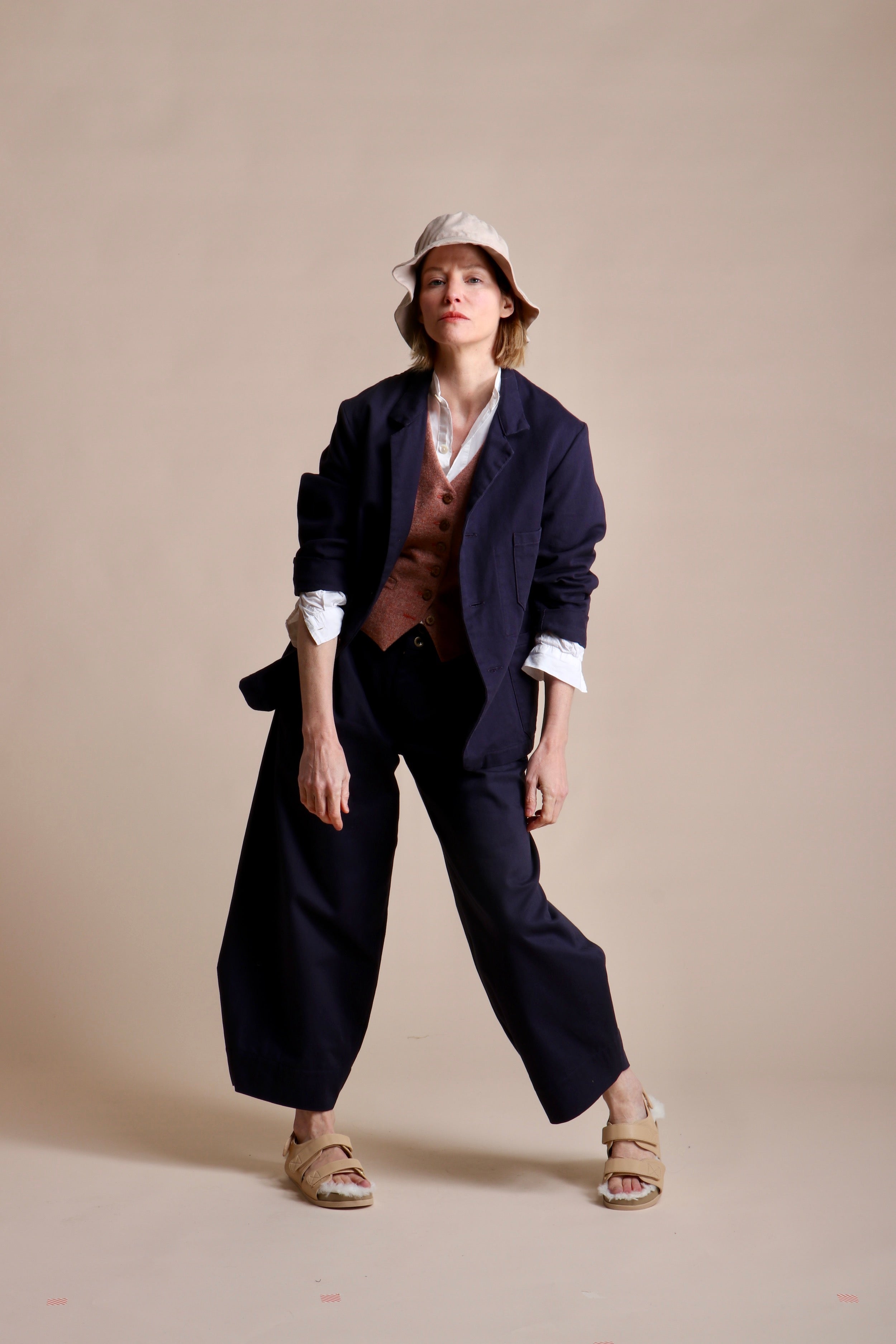 Woman wears Carrier Company 3 Button Jacket in Navy Drill with Dutch Trouser in Cotton, Lightweight Collarless Shirt and Wool Waistcoat in Coral