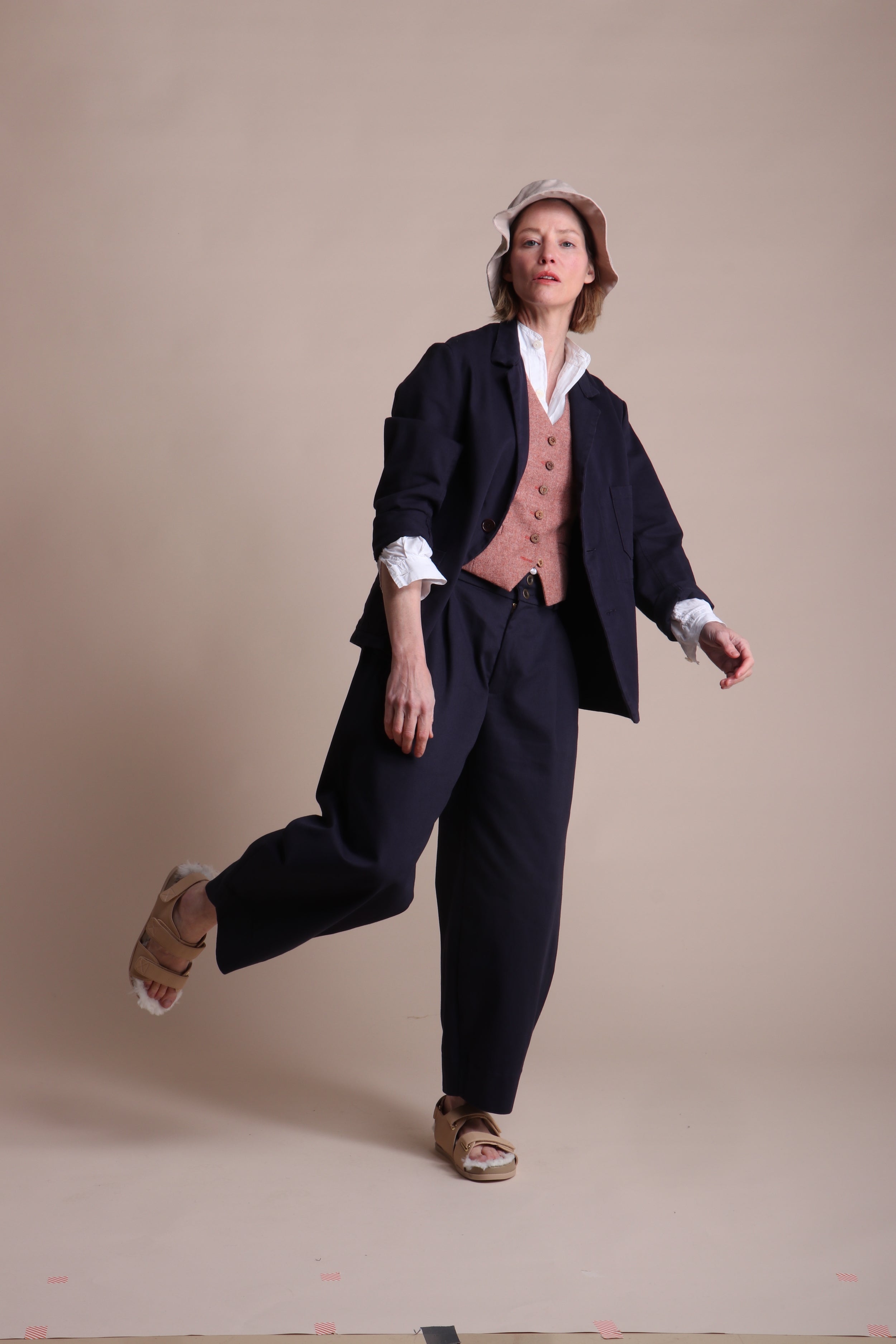 Woman wears Carrier Company 3 Button Jacket in Navy Drill with Dutch Trouser in Cotton, Lightweight Collarless Shirt and Wool Waistcoat in Coral