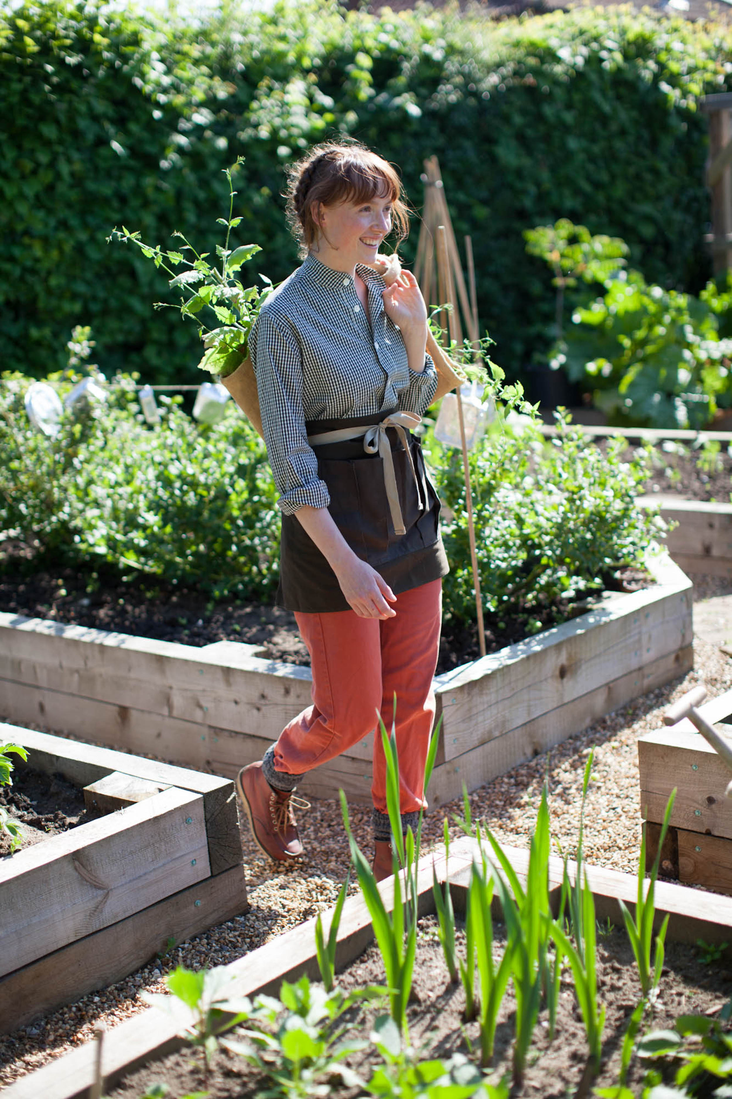 Woman wears Carrier Company Collarless Work Shirt in Black Cotton with Gardener's Half Apron and Women's Work Trouser in Orange