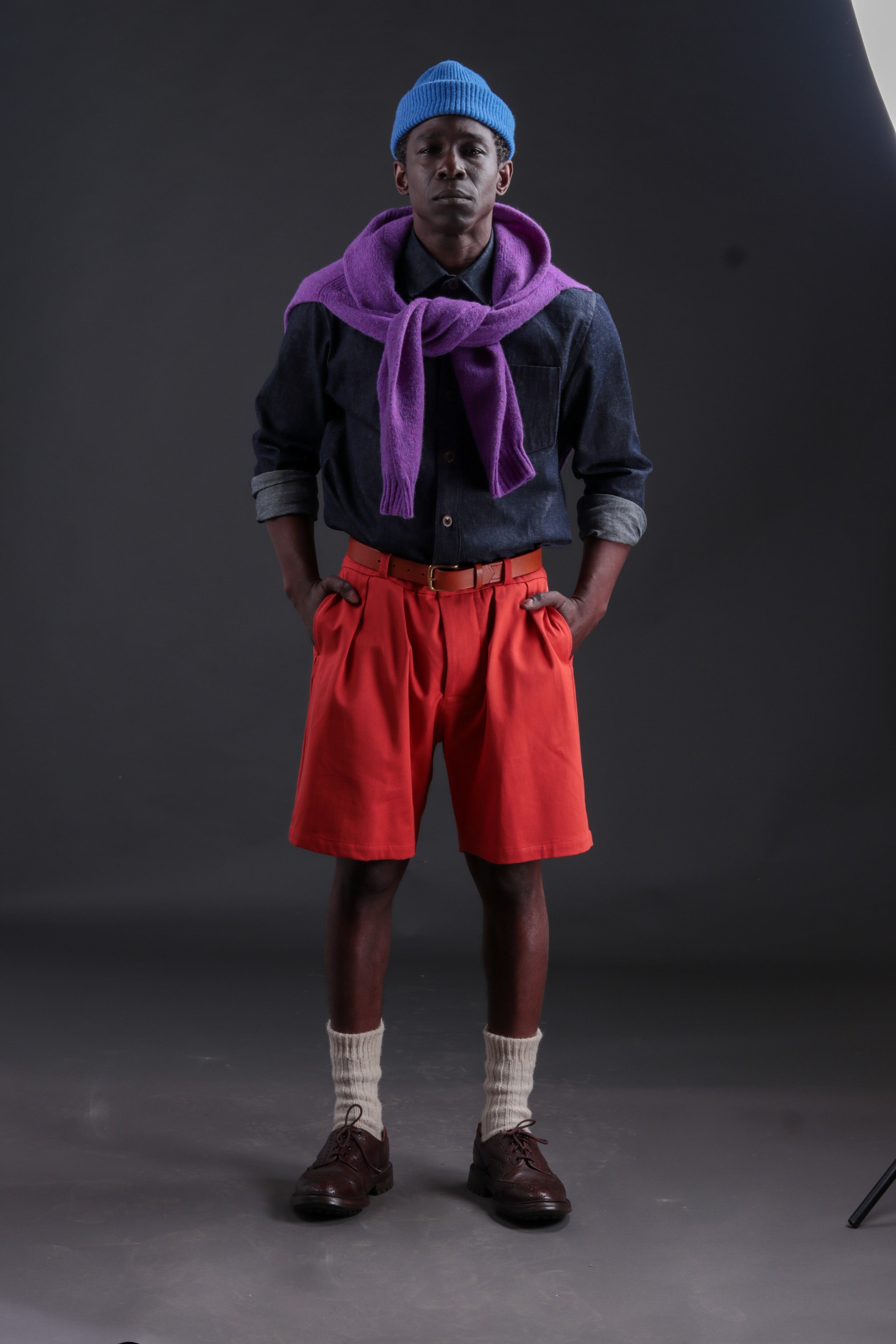 Man wears Carrier Company Shetland Lambswool Jumper in Allium with Denim Collar Shirt, Leather Belt, grandpa Shorts in Orange and Donegal Socks