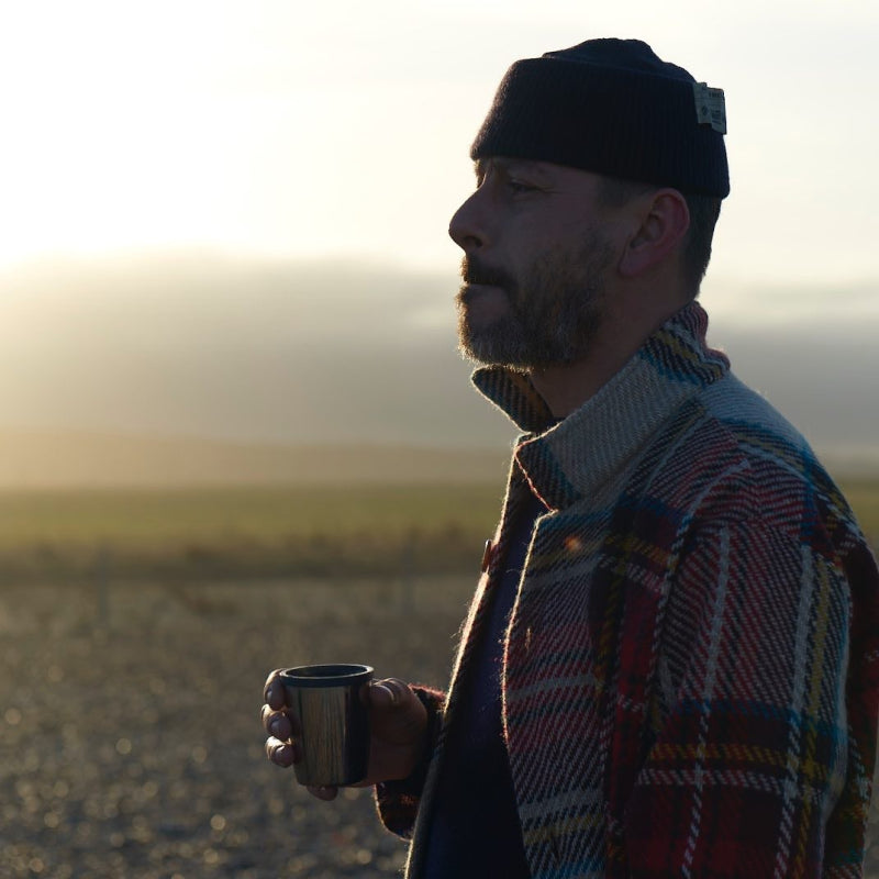 Man wearing the red Carrier Company Celtic Wool Jacket with a black hat drinking hot coffee outside