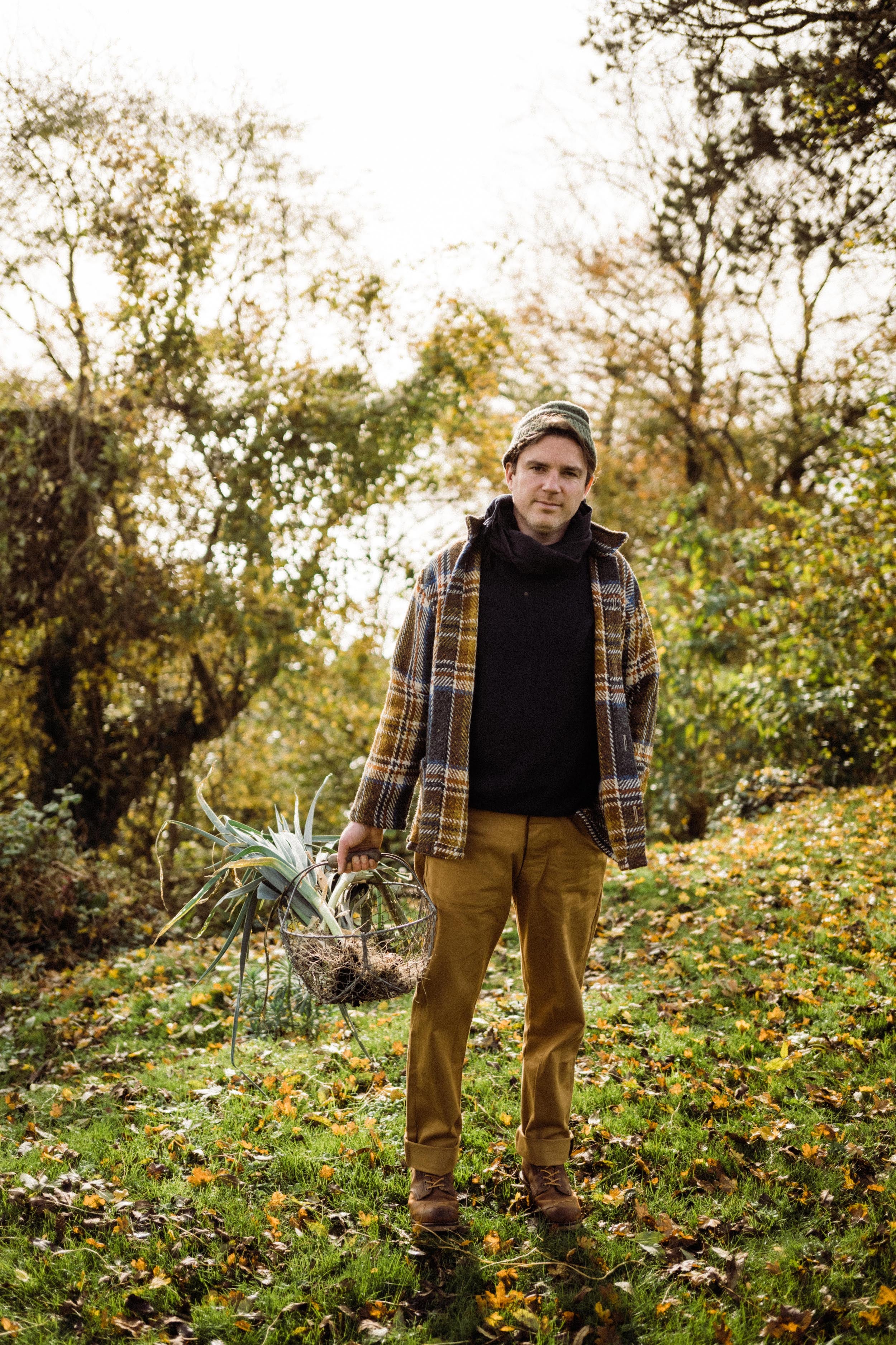 Man wears Carrier Company Celtic Wool Jacket in Slate & Russet with Traditional Guernsey and Men's Work Trouser in Tan