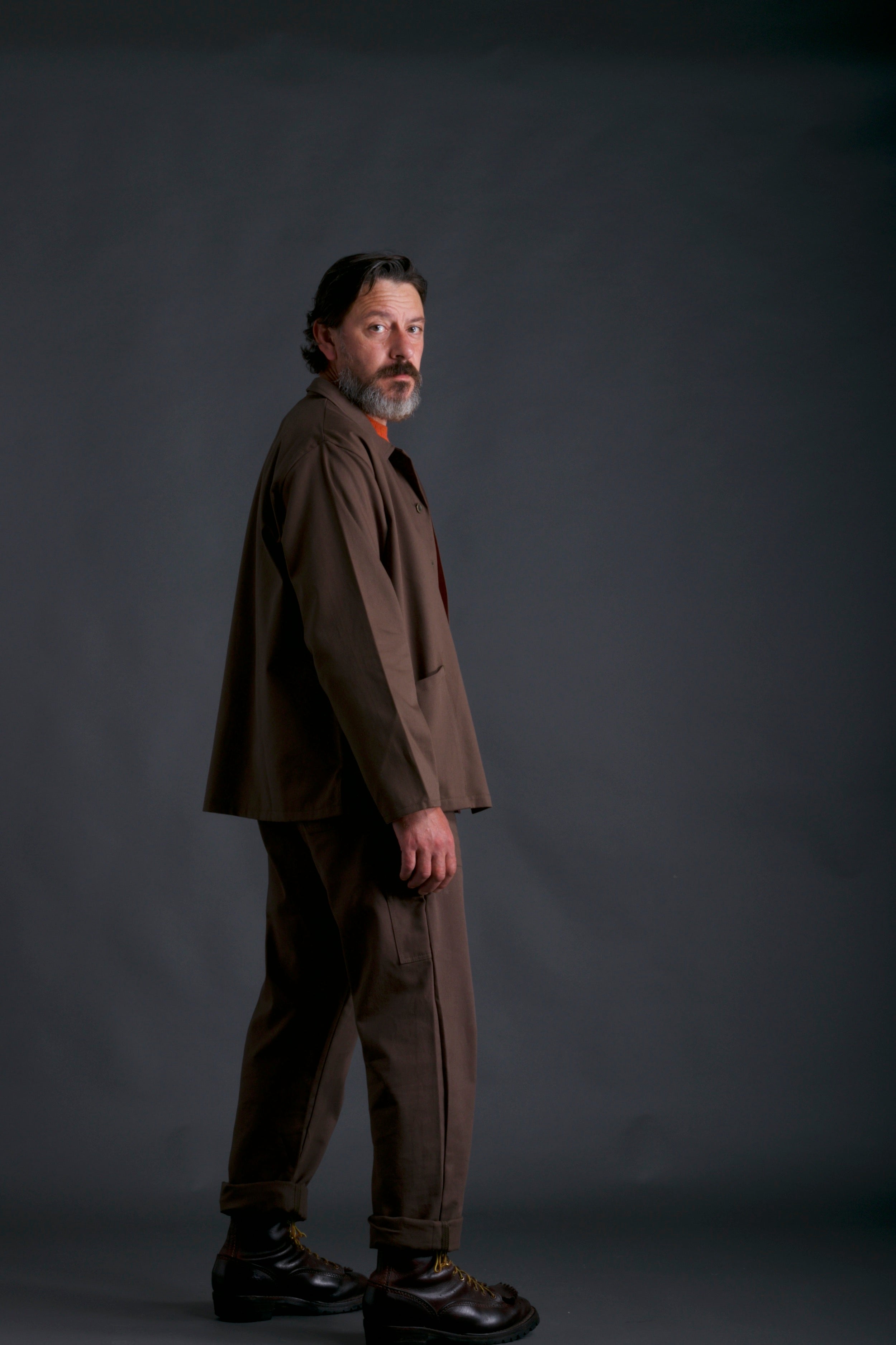 Man wears Traditional Work Jacket in Olive with Olive Dungarees and Tangerine Lambswool Jumper