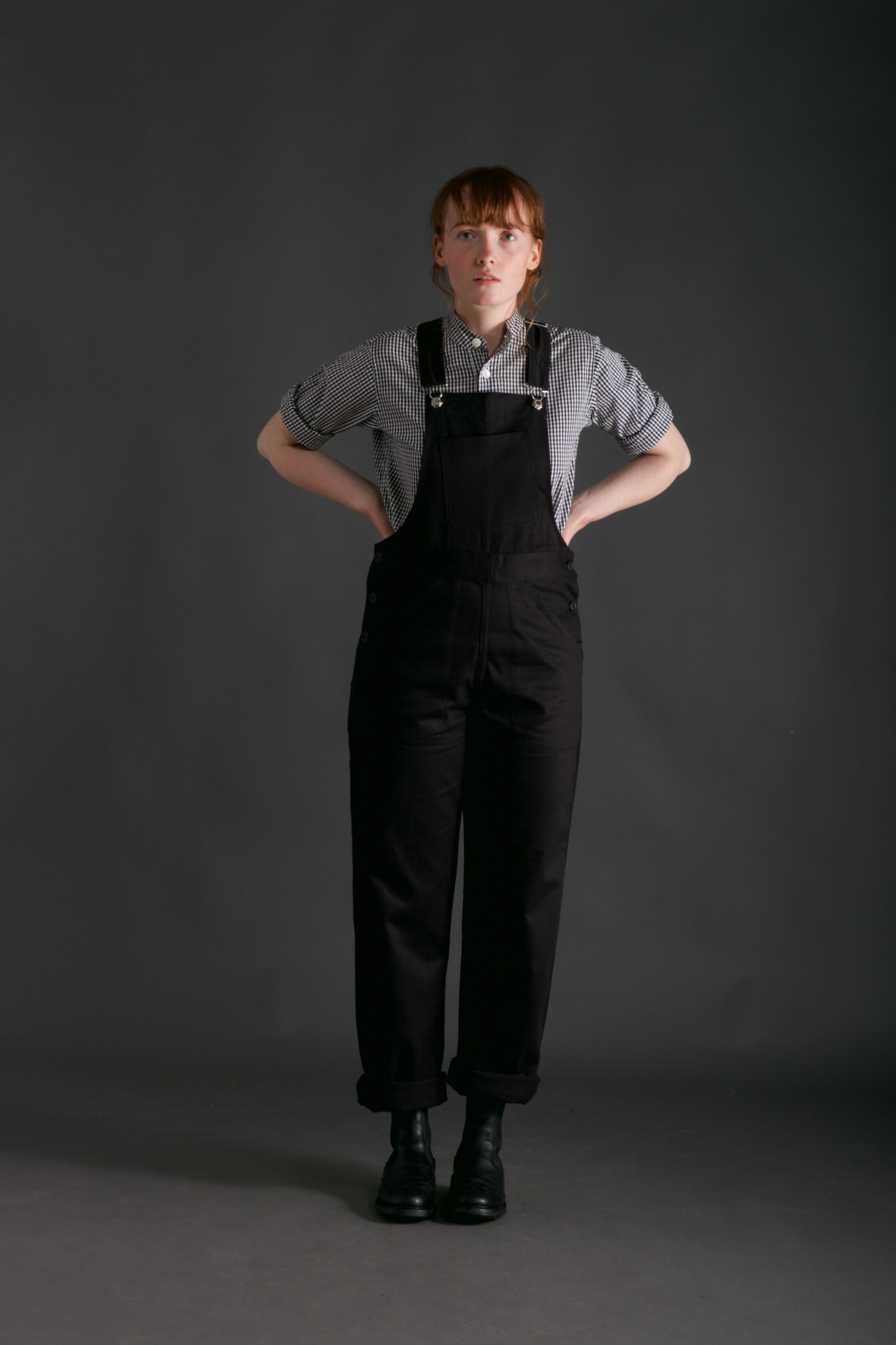 Woman wears Carrier Company Women's Dungarees and Organic Cotton Collarless Shirt in Black Gingham