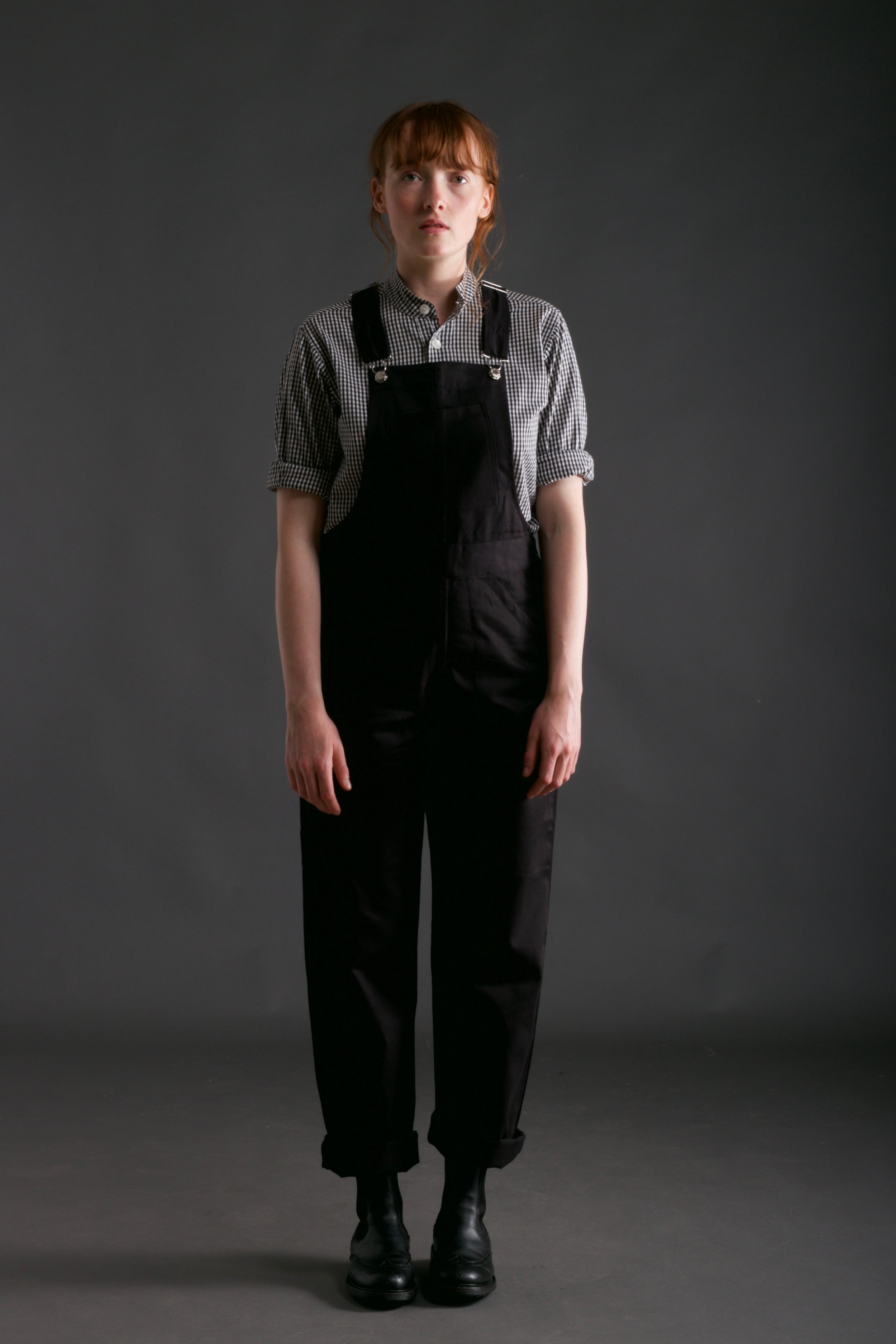 Woman wears Carrier Company Women's Dungarees and Organic Cotton Collarless Shirt in Black Gingham