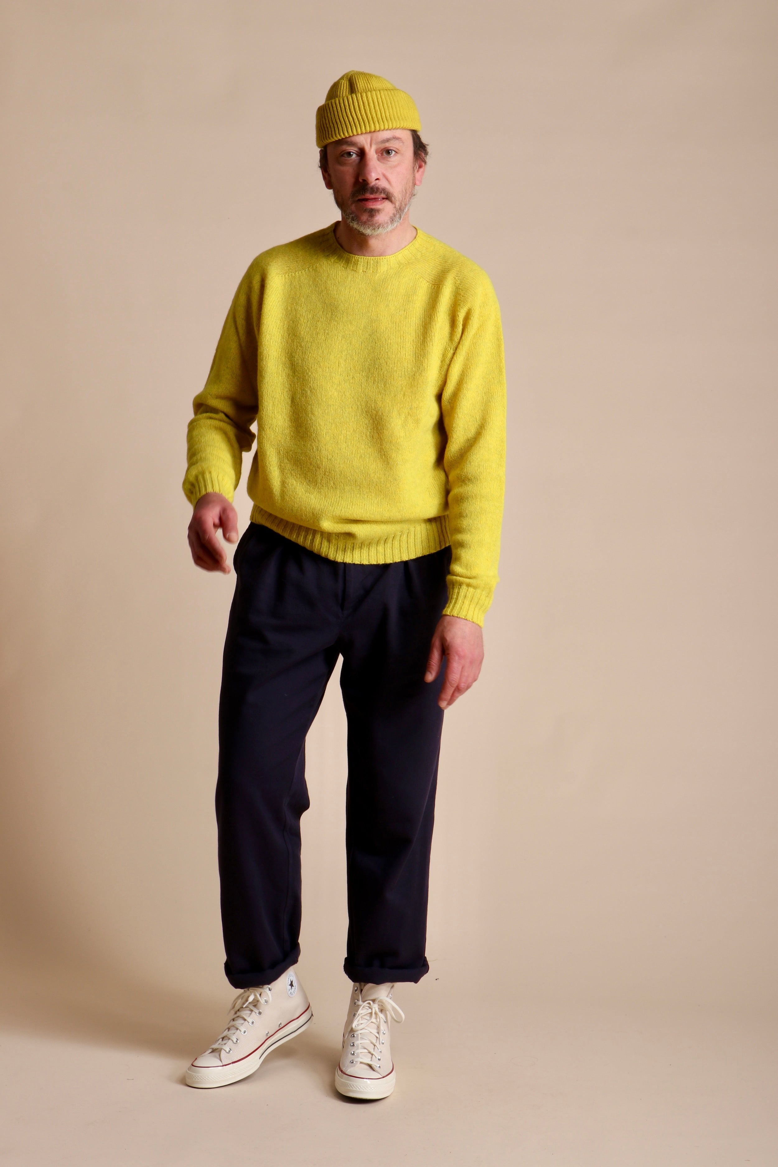 Man wears Carrier Company Classic Trouser in Navy Drill with Shetland Lambswool Jumper in Acid Yellow with Wool Hat in Yellow