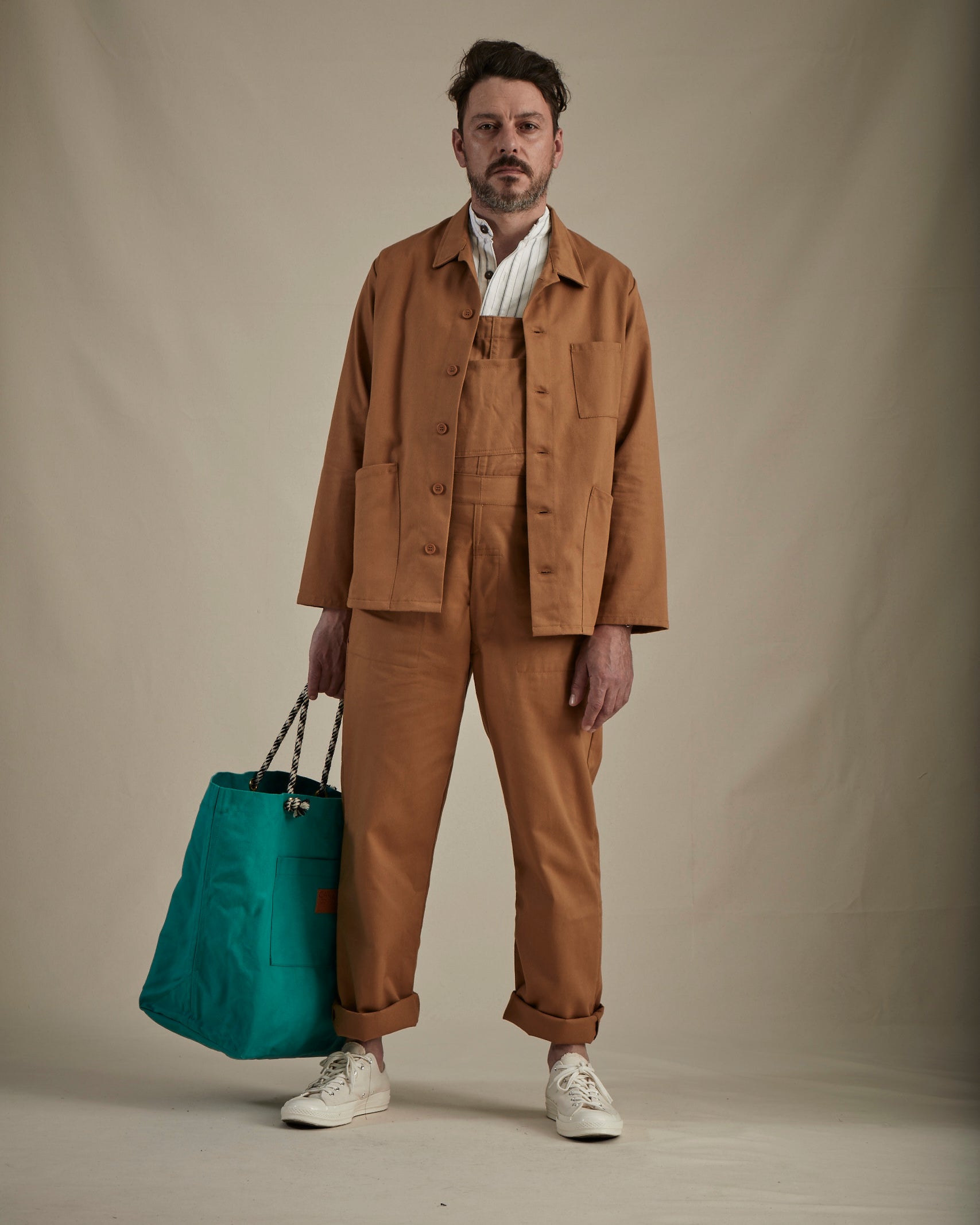 Man wearing the tan Carrier Company Men's Dungarees with a tan jacket and green bag
