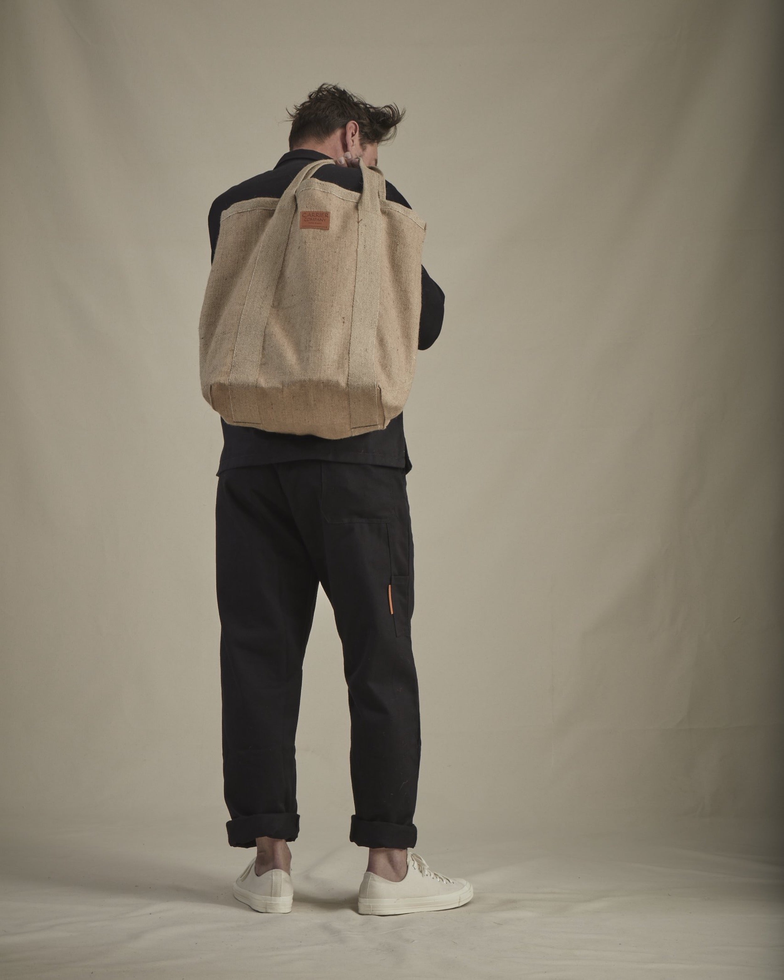 Man wearing Carrier Company Men's Work Trouser in Black and Holding Jute Market Bag