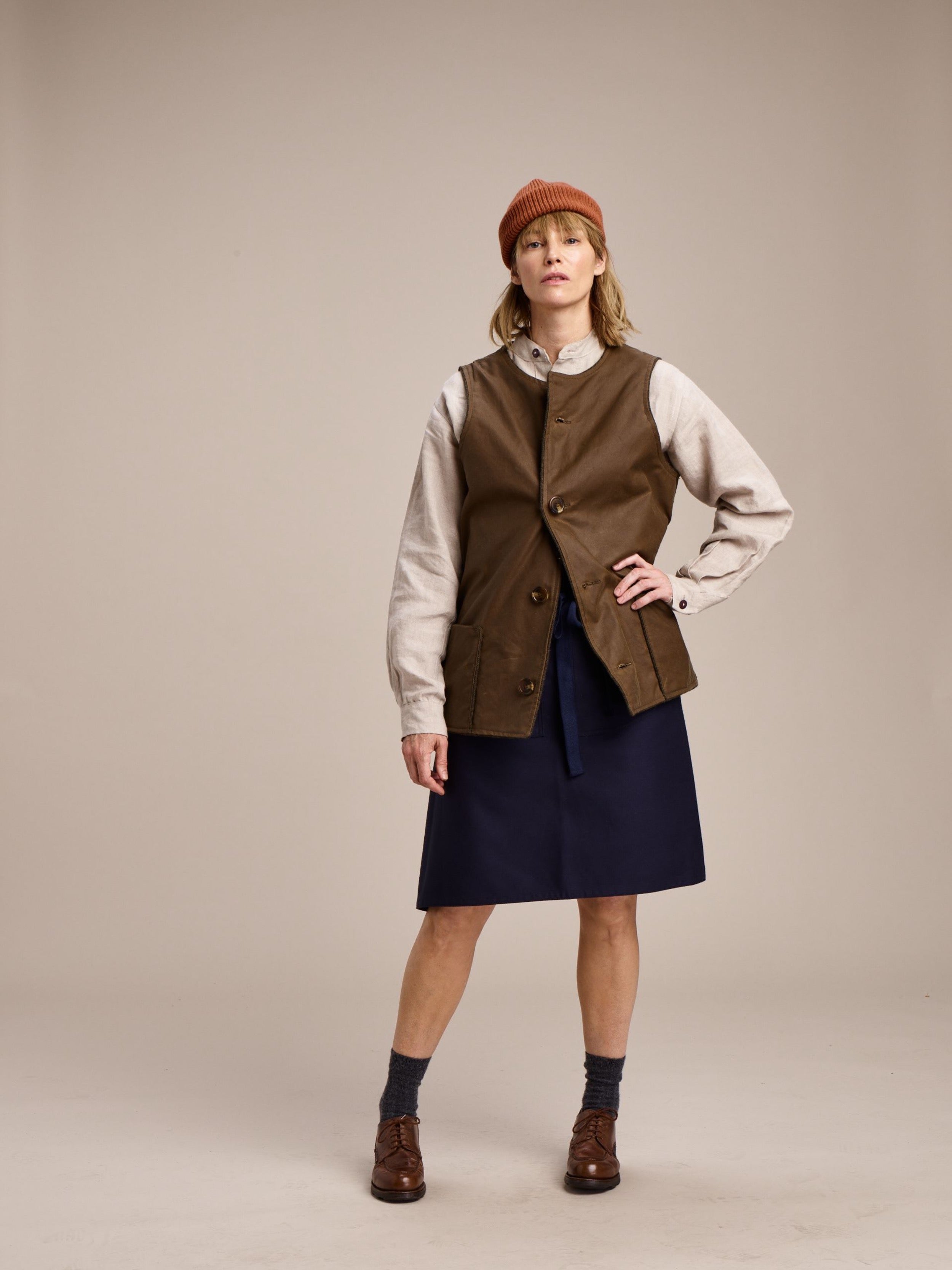 Woman wearing Carrier Company Norfolk Jerkin in Tan with Mum Skirt and Linen Collarless Work Shirt