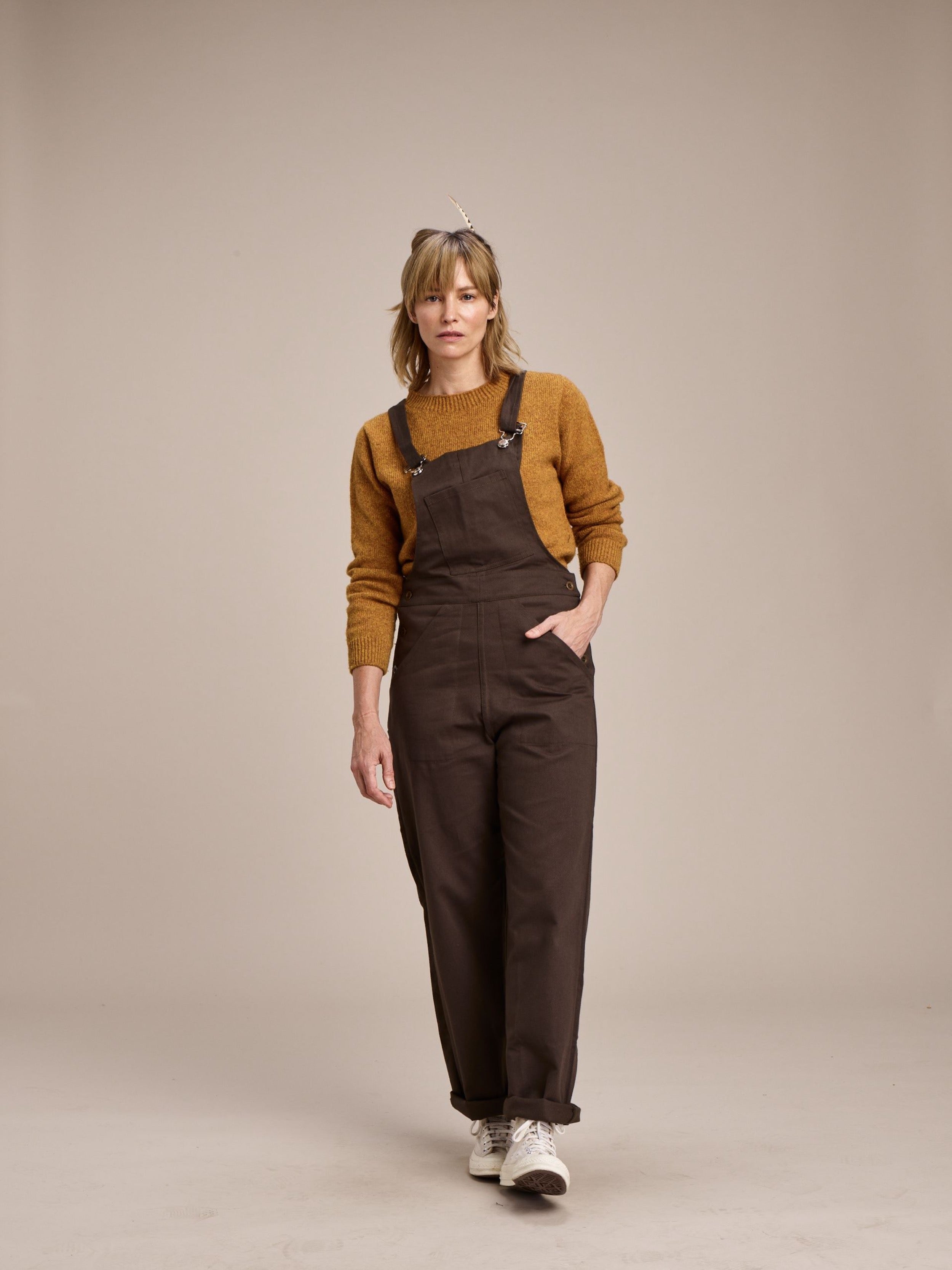 Woman wears Carrier Company Women's Dungarees in Olive with Shetland Lambswool Jumper