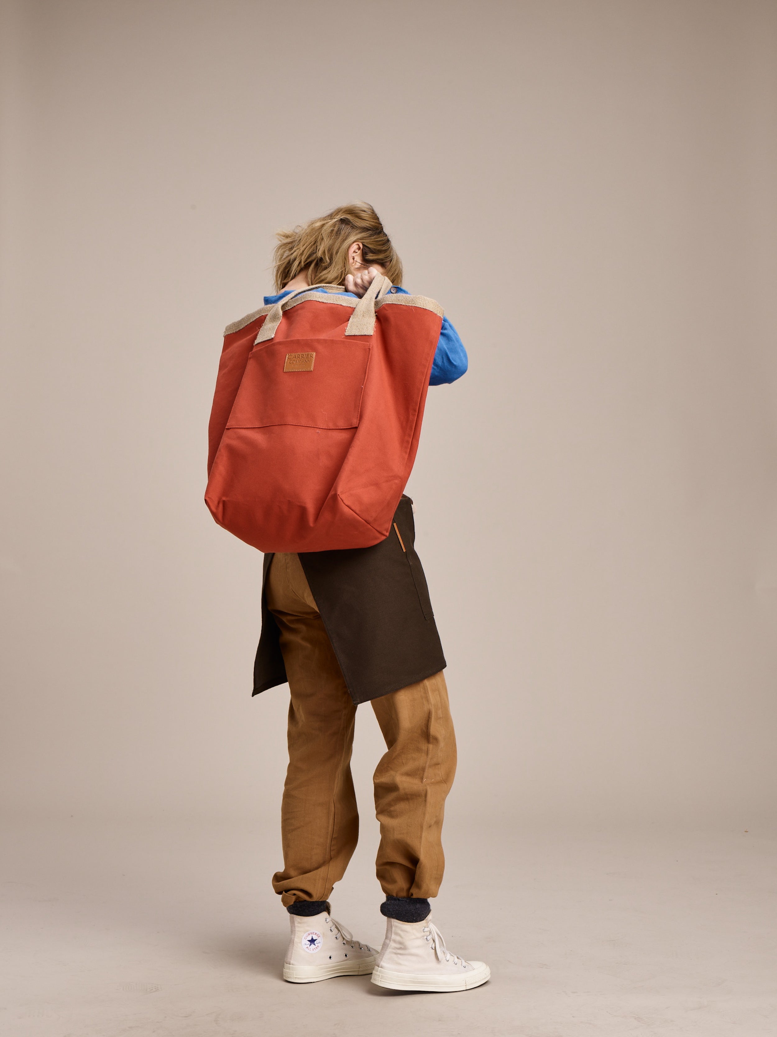 Woman wearing Carrier Company Women's Work Trouser in Tan with Linen Collarless Shirt and Half Apron holding Loot & Boot Bag