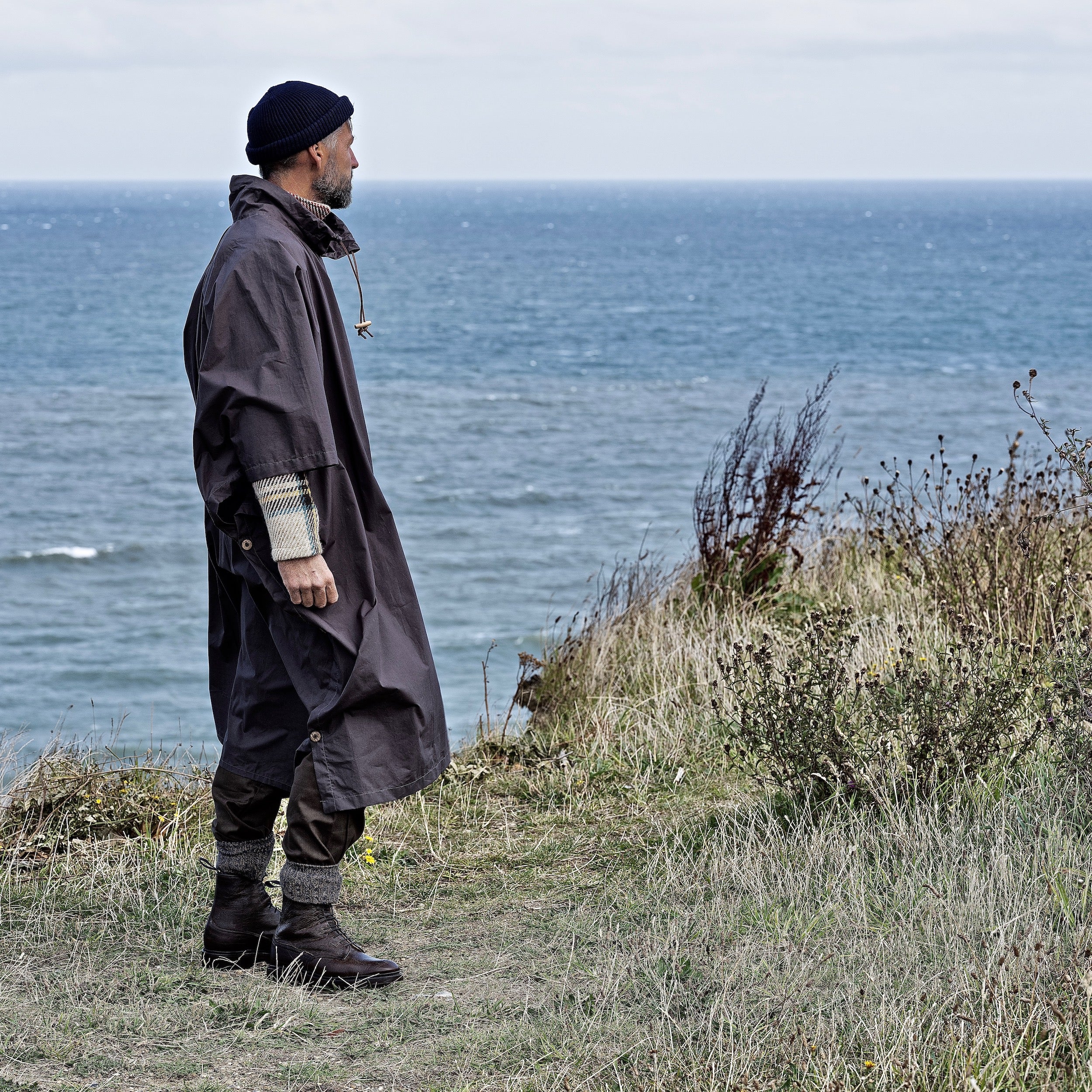 Man wearing the Carrier Company Long Rain Cape standing on a cliff overlooking the ocean