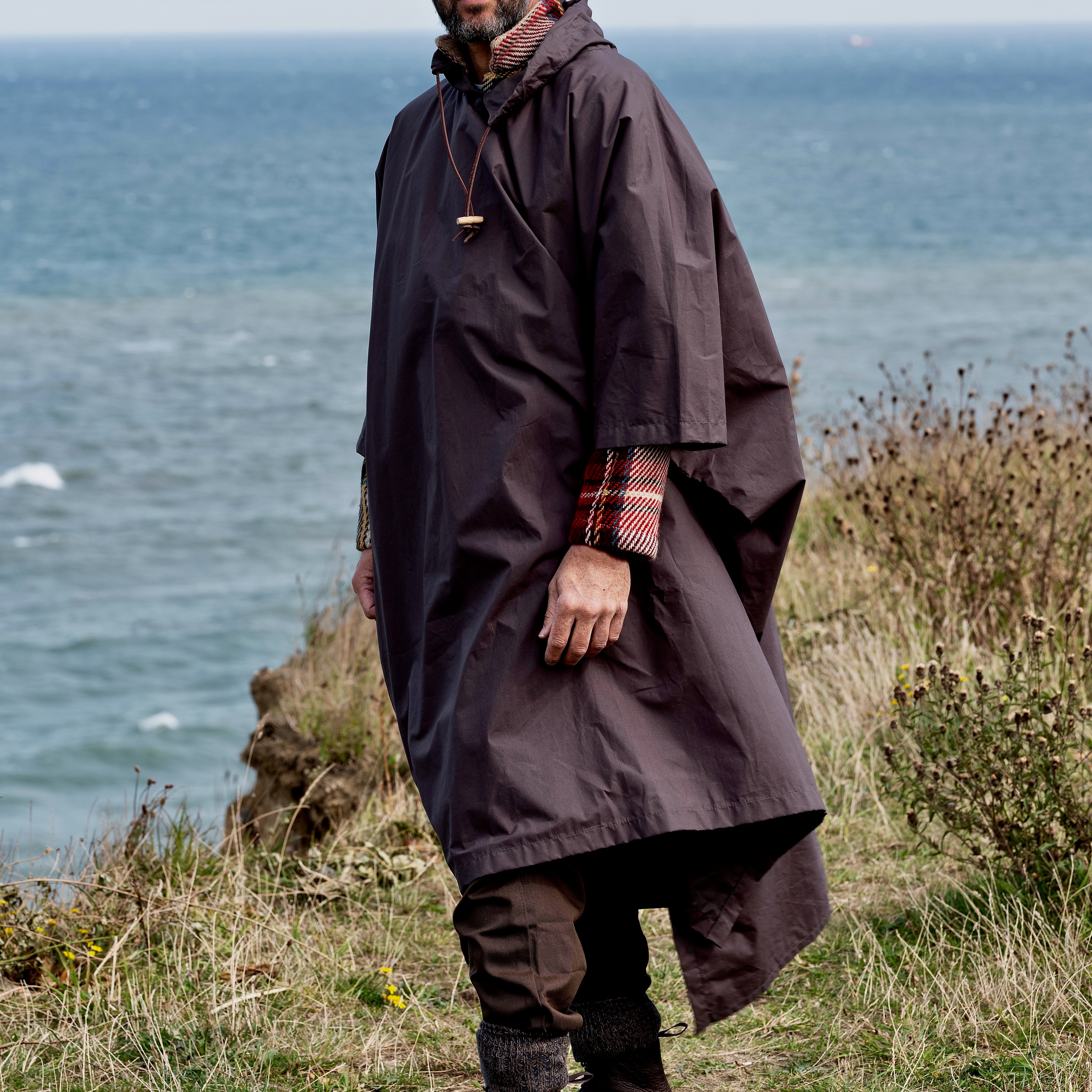Man walking along a cliff overlooking the ocean wearing the Carrier Company Long Rain Cape.