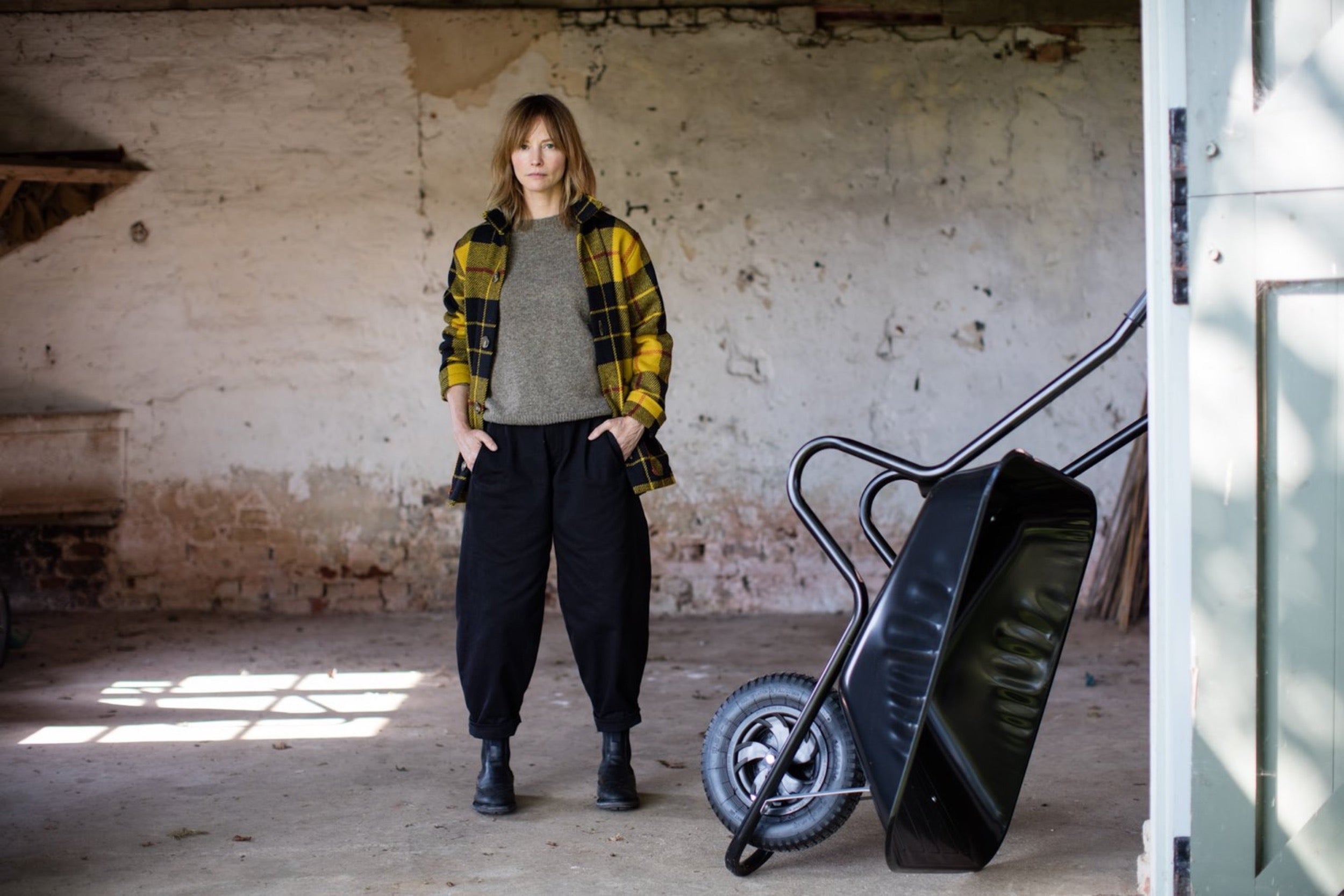 Woman in barn wearing Carrier Company Celtic Wool Jacket in Black and Yellow Check with Shetland Lambswool Jumper and Black Dutch Trouser in Cotton Drill