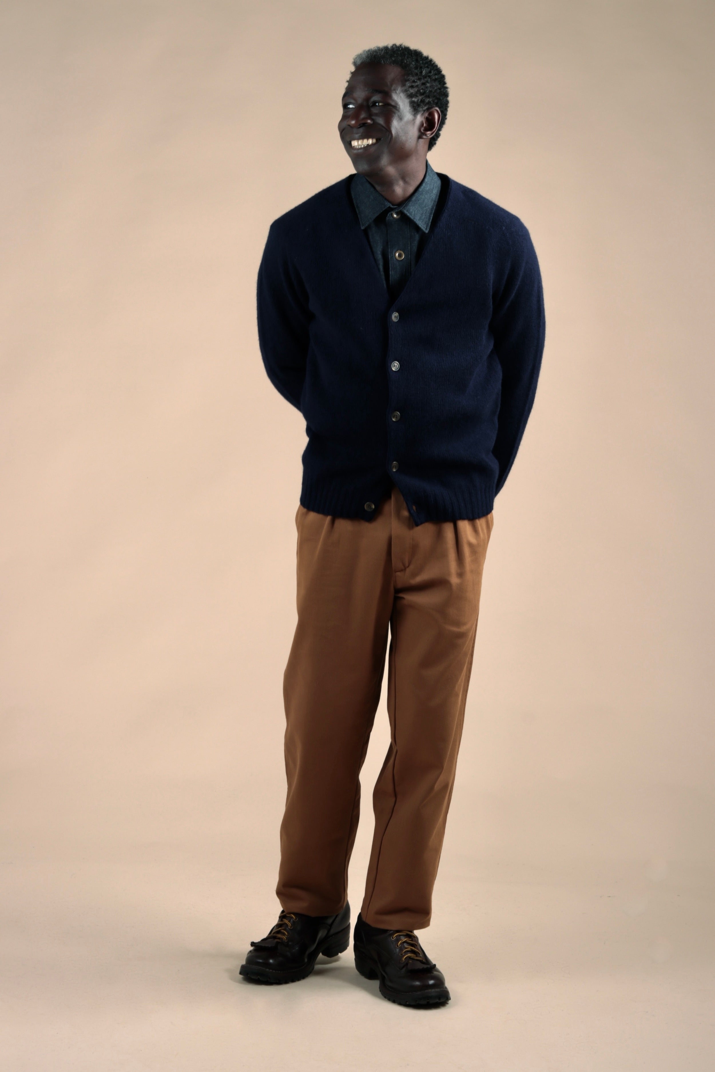Man wears Carrier Company Navy Cardigan with Denim Collar Shirt and Classic Trousers in Tan