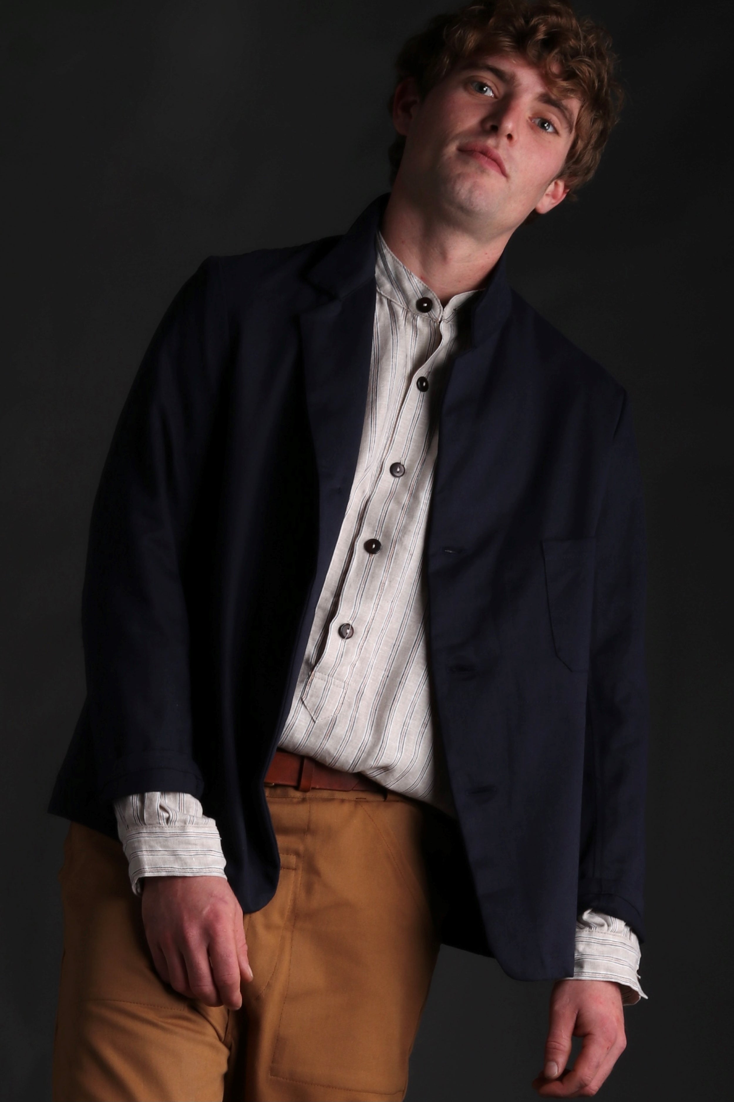 Man wears Carrier Company Collarless Shirt in Natural Linen with Three Button Navy Jacket and Tan Work Trousers