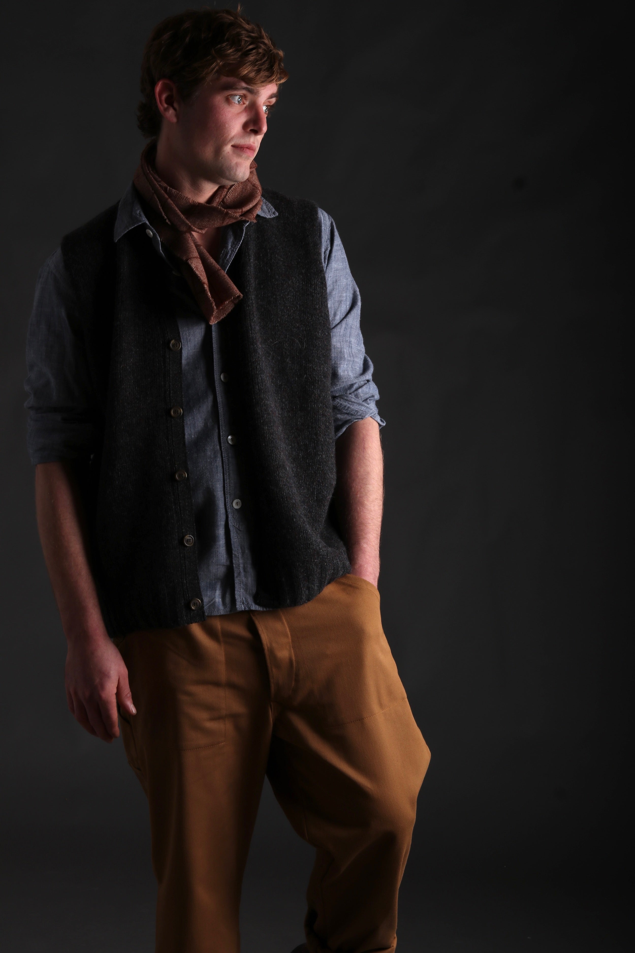 Man wears Carrier Company Sleeveless Cardigan with Chambray Shirt and Classic Trouser in Tan