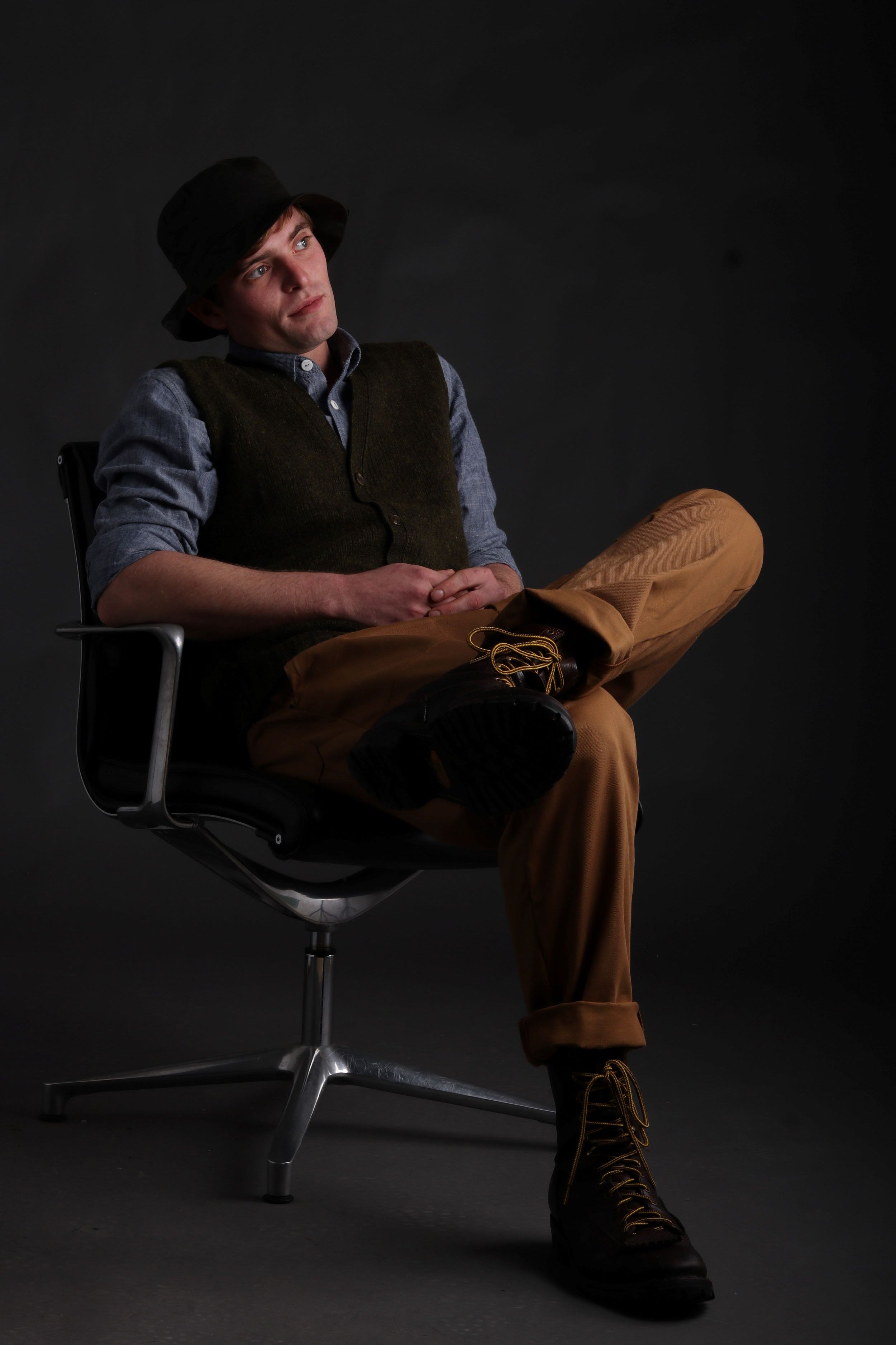 Man wears Carrier Company Rain Hat with Sleeveless Cardigan in Kale