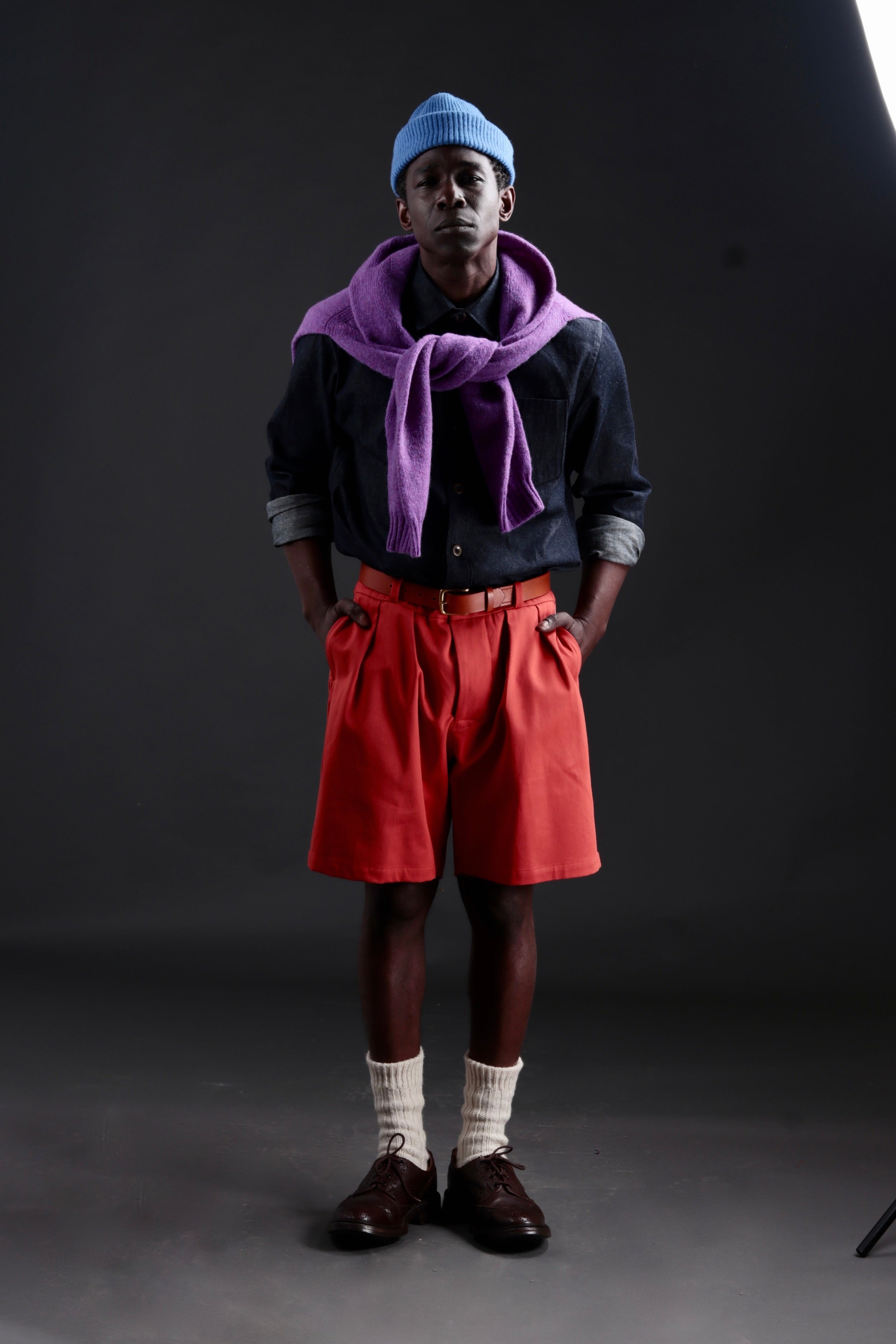 Abdul wears Carrier Company Grandpa Short in Orange with Denim Collar Shirt, Shetland Lambswool Jumper in Allium and Wool Hat