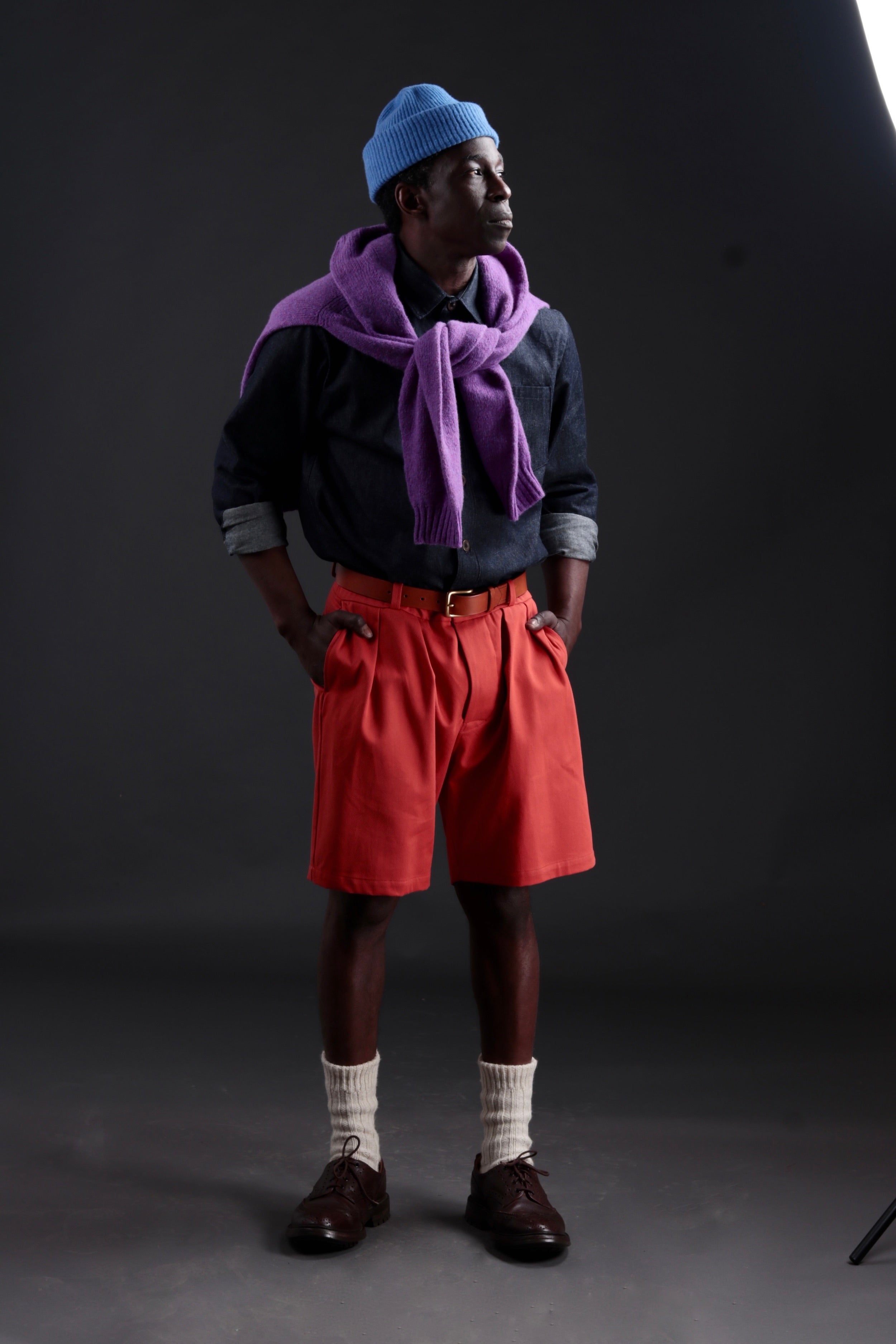 Abdul wears Carrier Company Grandpa Short in Orange with Denim Collar Shirt, Shetland Lambswool Jumper in Allium and Wool Hat